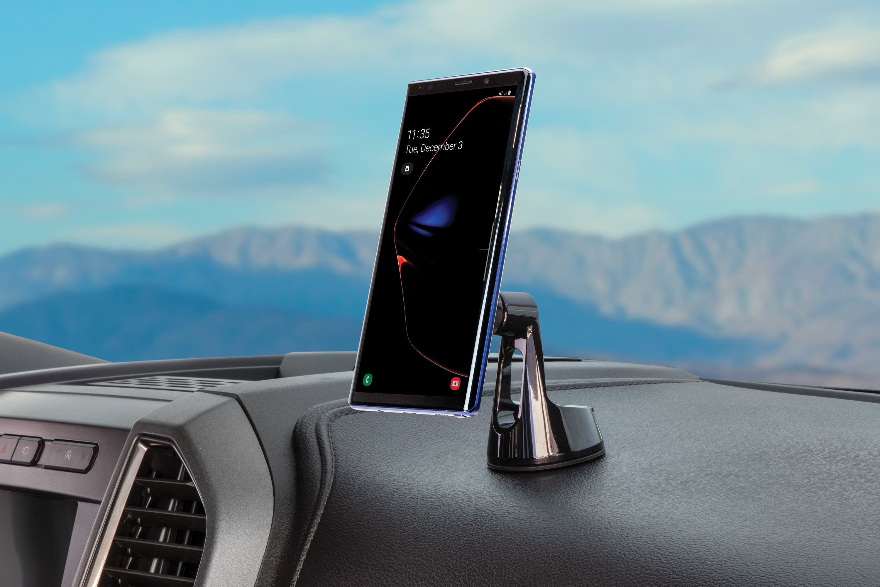 The image shows a car's dashboard with a cell phone mounted on it. The phone is positioned in a holder, and the time displayed on the phone is 11:35. The date is December 3. The car is parked, and the dashboard is clean and well-organized.