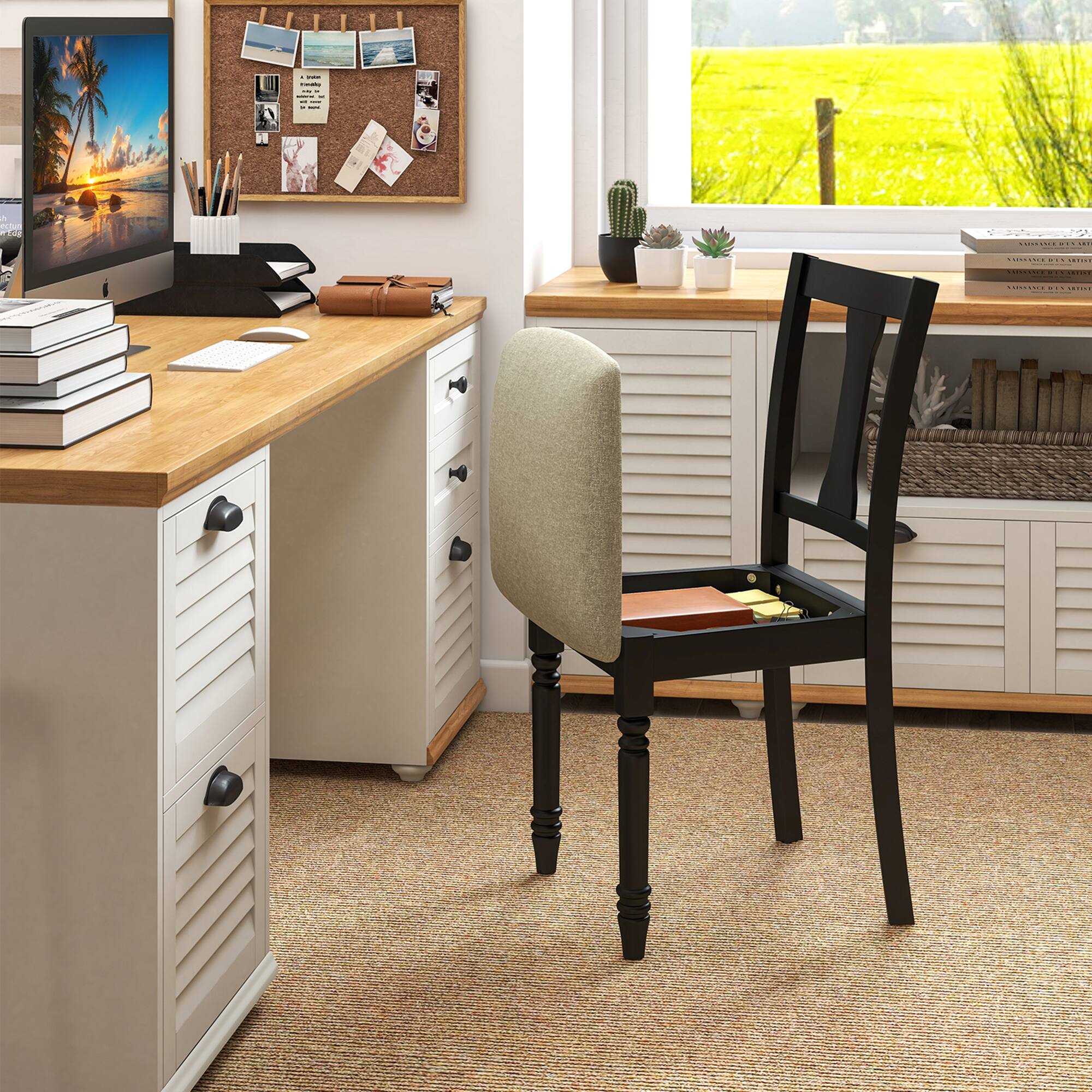 The image shows a well-organized home office setup. A wooden desk with a light-colored finish is positioned against a wall, featuring a computer monitor displaying a beach scene. On the desk, there are several items including a stack of books, a keyboard, a mouse, a pen holder with pens and pencils, and a brown leather-bound notebook. Above the desk, a corkboard is mounted on the wall, adorned with various notes and photos. To the right of the desk, a black chair with a cushioned seat and backrest is placed, and beneath it, a small drawer is open, revealing some papers. The room has a large window that offers a view of a green field outside. On the windowsill, there are a few potted plants and more books. The floor is carpeted, and the overall ambiance is neat and inviting.