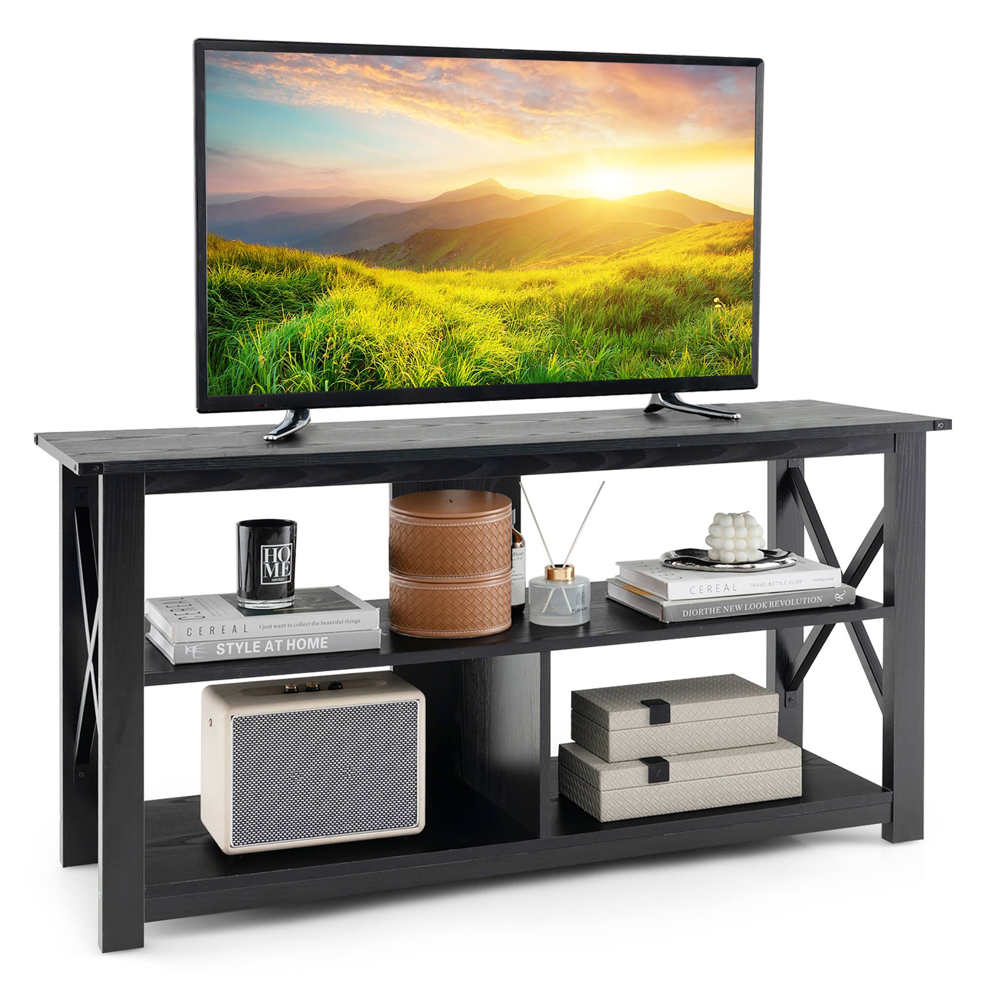 The image features a television placed on a wooden stand. The stand has a shelf underneath the television, which is filled with various items. There are three books on the shelf, with one of them being a cookbook. Additionally, there are two cups, a remote control, and a vase on the shelf. The television is turned on, displaying a beautiful sunset scene.