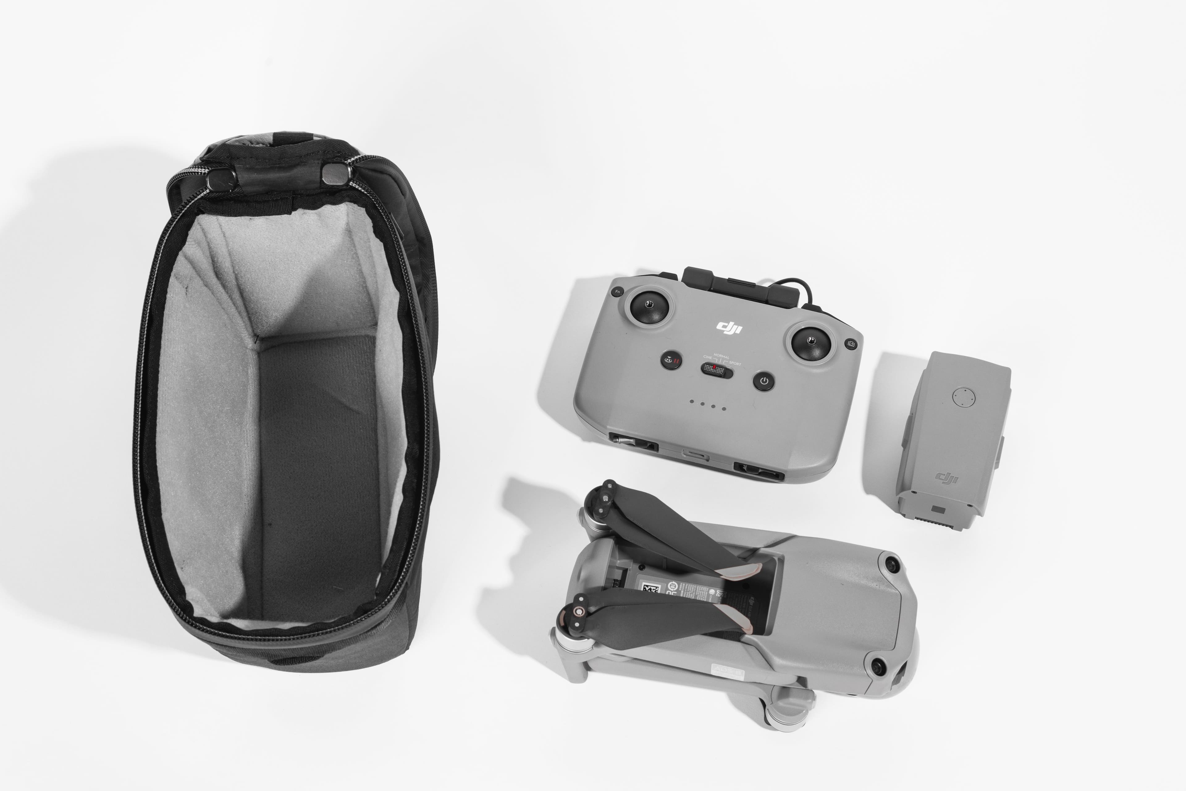 The image shows a grey and black drone with a controller and a carrying case. The drone is in the process of being assembled, with its parts laid out on a white background. The controller is placed next to the drone, while the carrying case is located nearby. The drone appears to be a small, portable device, perfect for outdoor activities and hobbies.
