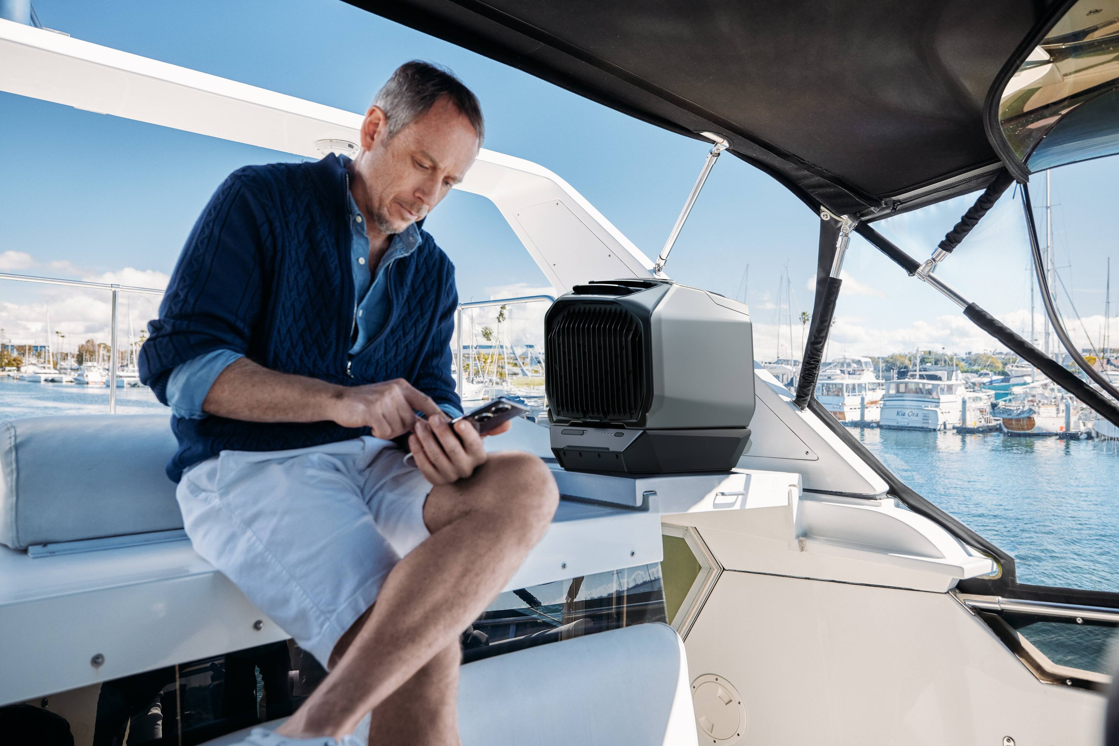 The man is sitting on a boat, looking at his cell phone.