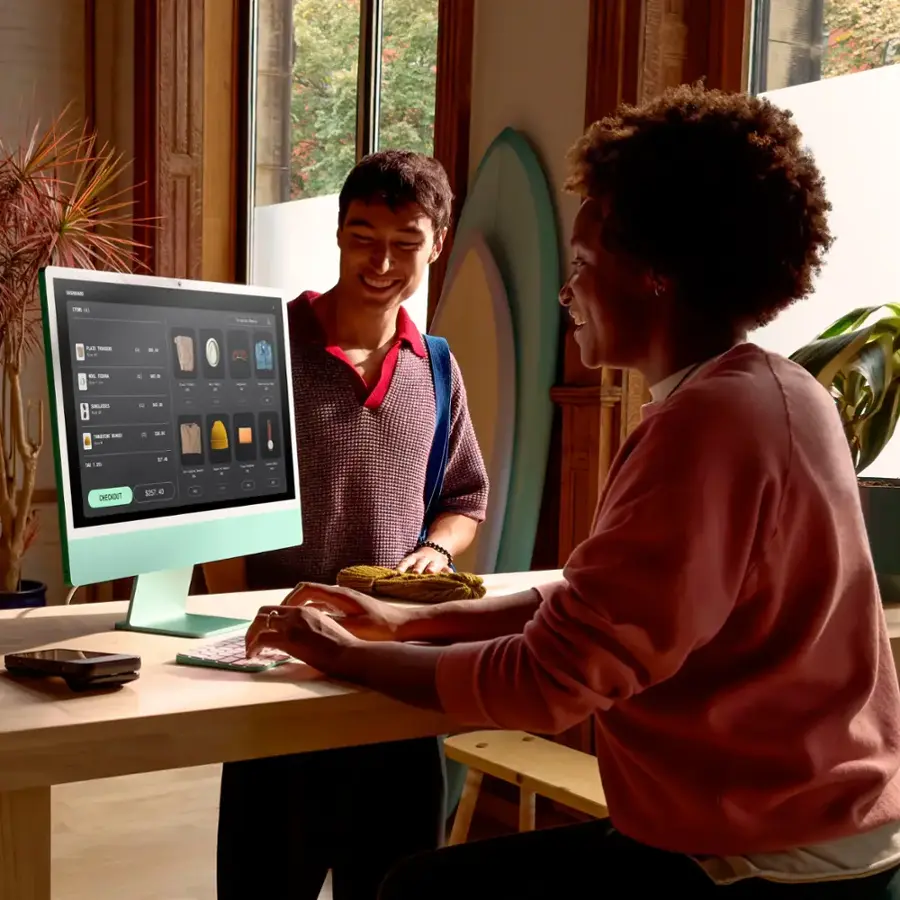 The image shows a man and a woman sitting at a table in front of a computer screen. The man is smiling and holding a plate of food, while the woman is looking at the screen. They are both engaged in a conversation or activity related to the computer. The scene suggests a casual and friendly atmosphere, with the man and woman enjoying their time together.