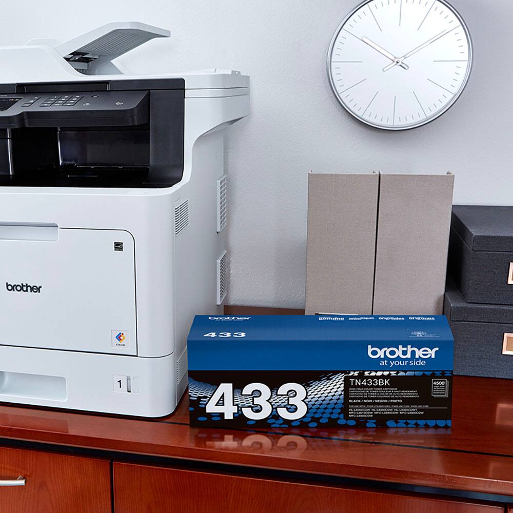 The image features a white Brother printer sitting on a desk. Next to the printer, there is a box of coffee and a clock. The clock is positioned above the printer, while the coffee box is placed below it. The scene suggests a workspace where the printer is used for daily tasks, and the coffee box provides a source of refreshment during work hours.