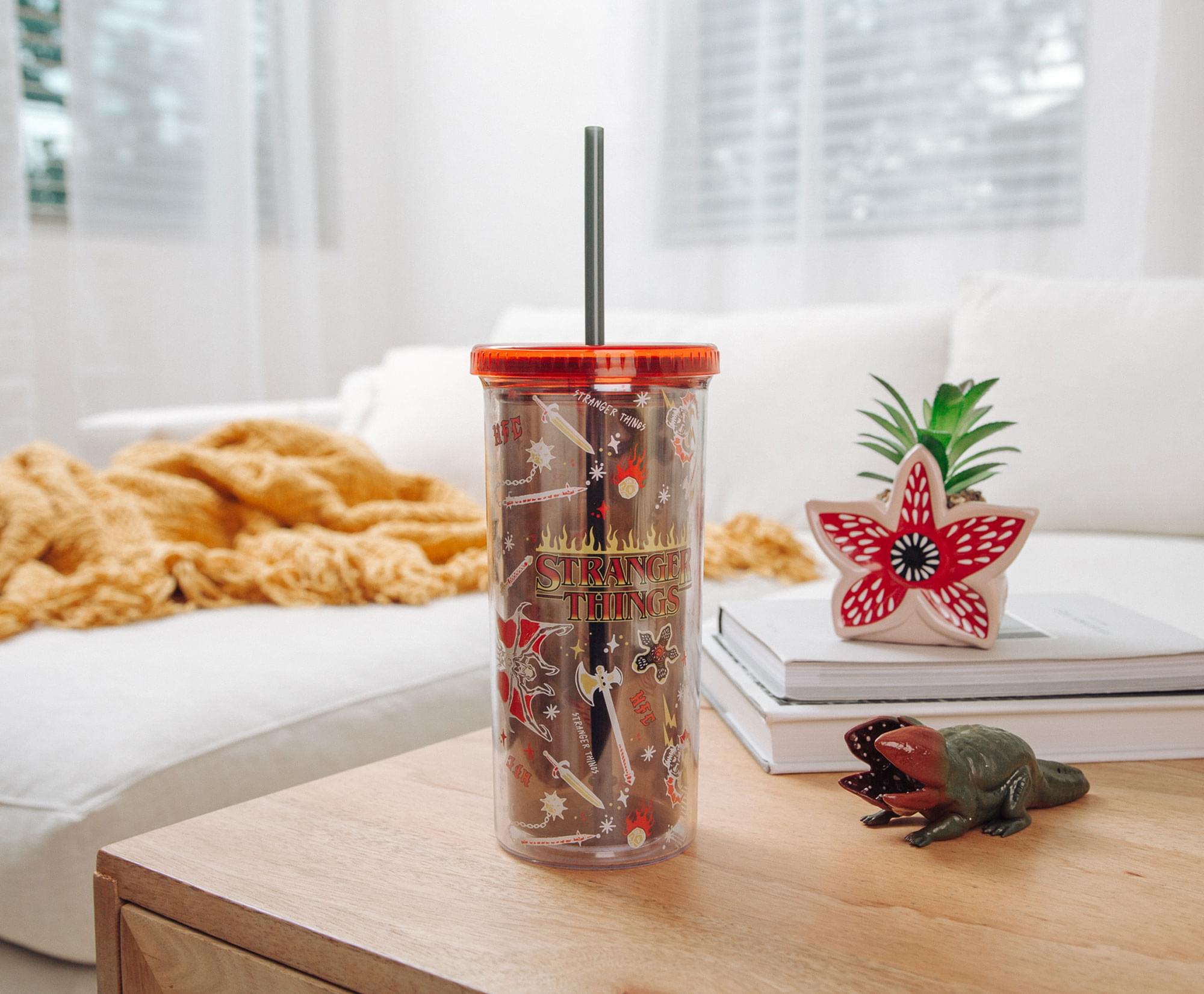 Sure, here is the corrected and grouped text from the image:

**On the Tumbler:**
- "STRANGER THINGS"
- "THE TOWER"
- "THE TOWER"
- "THE TOWER"

**On the Books:**
- "STRANGER THINGS"

**On the Pineapple Plant:**
- "STRANGER THINGS"

**On the Crocodile Toy:**
- "STRANGER THINGS"