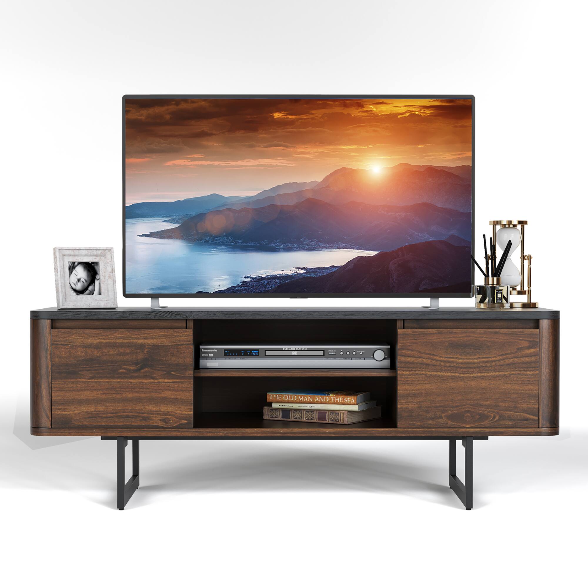 The image features a flat screen TV placed on a wooden stand. The TV is displaying a beautiful sunset scene. On the stand, there is a book and a picture frame, adding to the overall aesthetic of the setup. The TV stand is positioned in front of a window, allowing for natural light to illuminate the space.