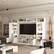 The living room is white and has a large flat screen TV on the wall. There are shelves on either side of the TV, and a couch is positioned in front of it. The room also features a coffee table and a potted plant. The living room is well-decorated with a variety of books and vases, creating a cozy and inviting atmosphere.