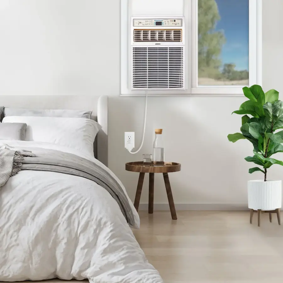 The image shows a bedroom with a bed, a table, and a potted plant. The bed is covered with a white comforter, and there is a window nearby. The table has a bottle and a vase on it, and a remote control is also present in the room. The potted plant is placed near the window, adding a touch of greenery to the space. The overall atmosphere of the room appears to be clean and organized, with a focus on simplicity and functionality.