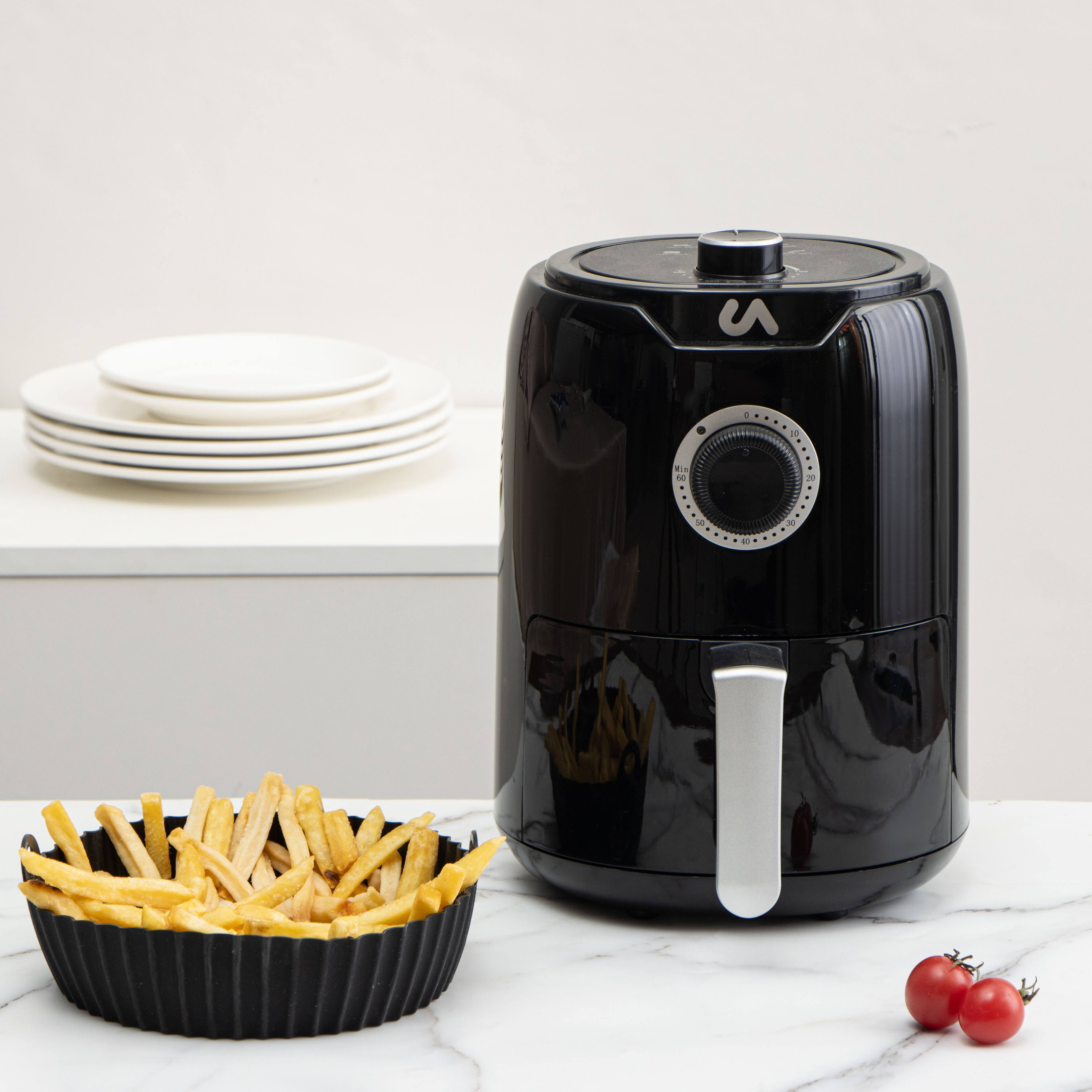 The text on the image is not clearly visible, so I cannot provide a correction. However, the image shows a black air fryer with a basket of fries and some cherry tomatoes on a marble surface. There are also plates stacked on a shelf in the background.