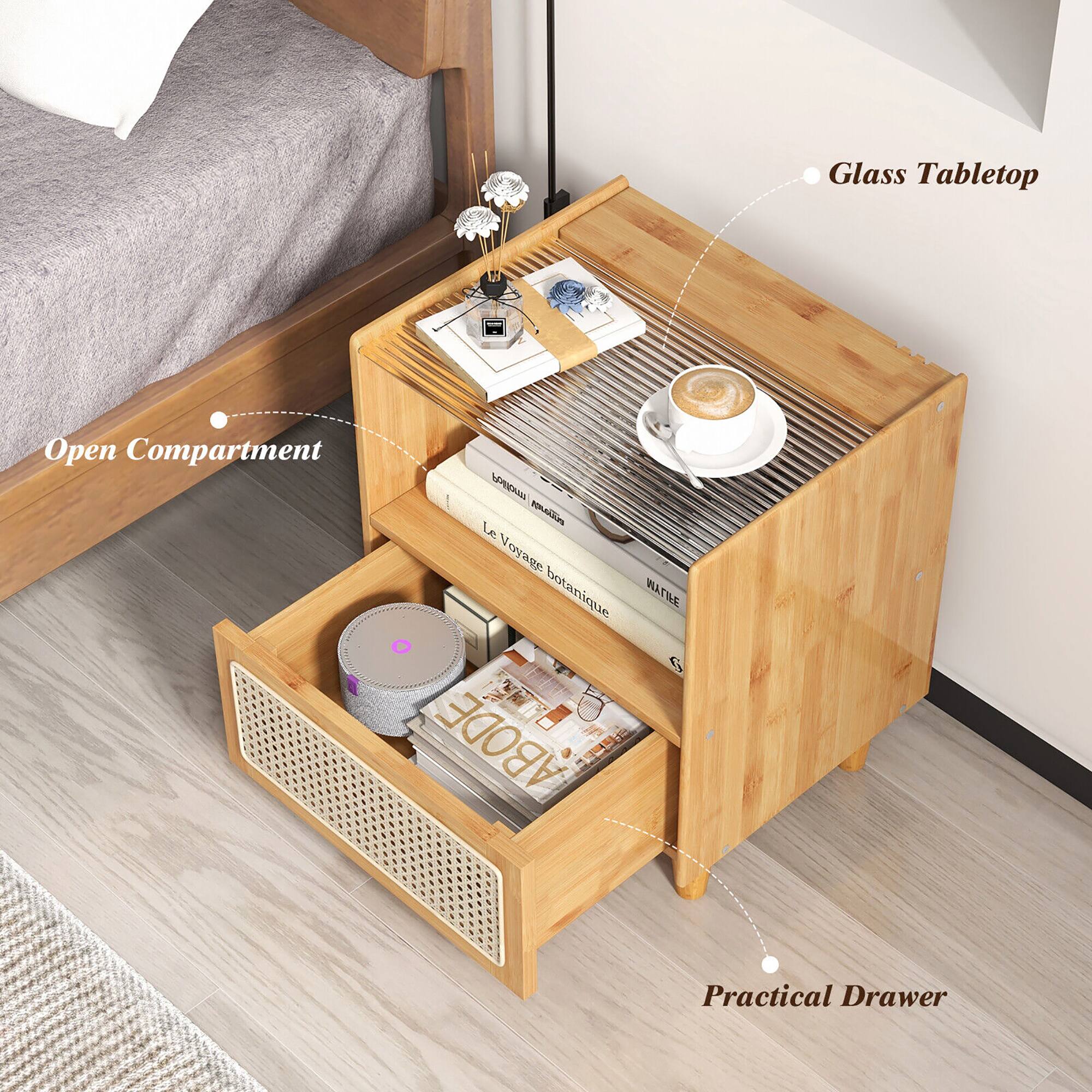 The image features a wooden table with a glass tabletop. The table has a compartment that is open, revealing a collection of books and magazines. There is also a coffee cup on the table, and a bed can be seen in the background. The table is described as a practical drawer, and it is likely used for storage or organization purposes.