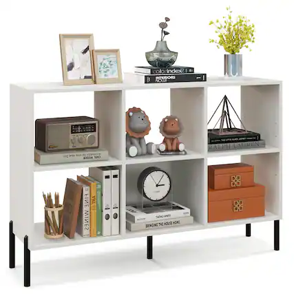 The image features a white shelf with various items on it. There are two books, one of which is titled "Interiors" and the other is titled "Architecture." In addition, there are two teddy bears on the shelf, one of which is brown and the other is gray. A clock is also present on the shelf, along with a vase and a potted plant. There is a picture frame on the shelf as well, adding to the overall decorative elements of the space.
