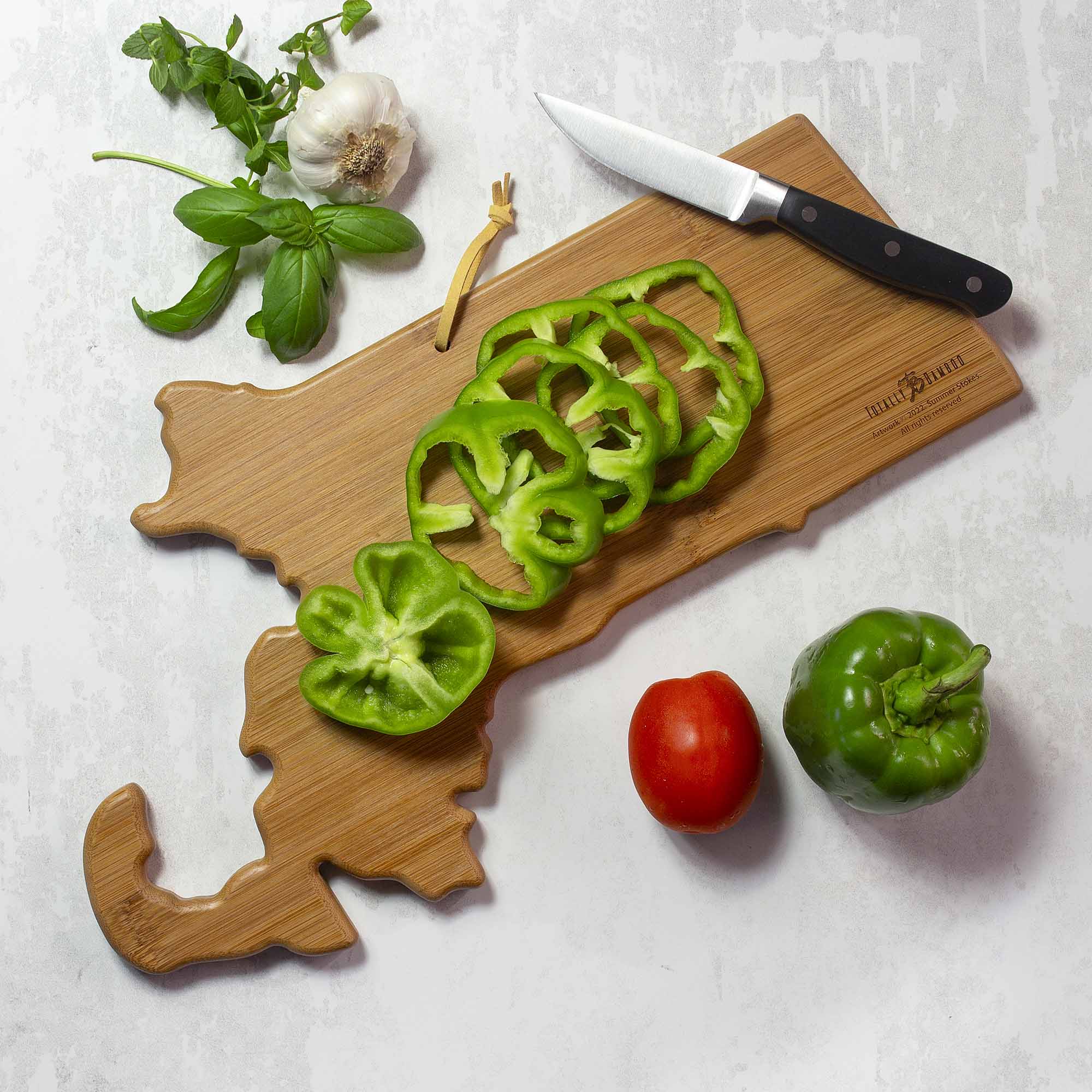 It's a picture of a cutting board with sliced green bell pepper, a whole green bell pepper, a tomato, garlic, basil, and a knife.