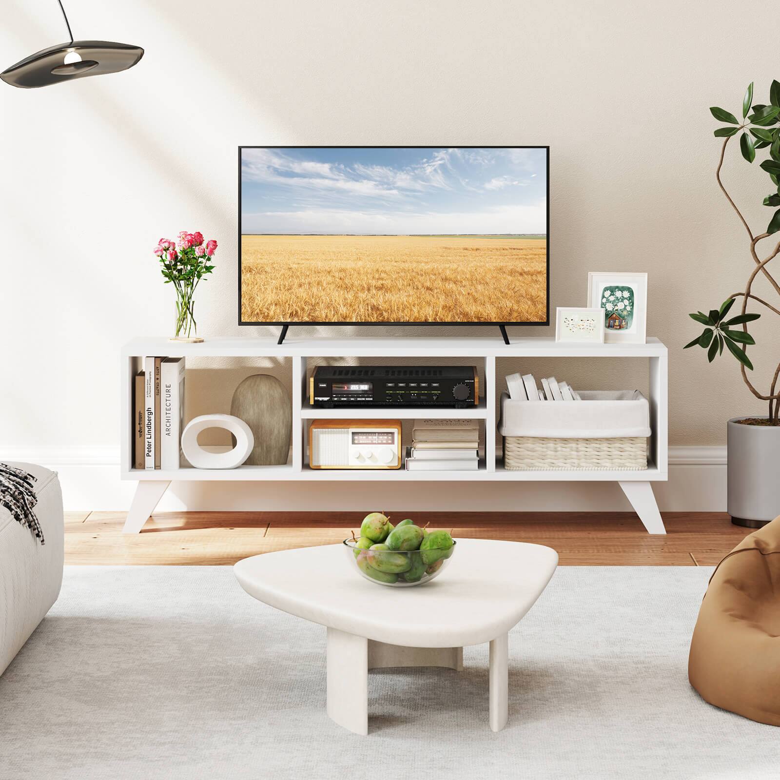 The image features a living room with a large flat screen TV mounted on the wall. The room is furnished with a couch, a coffee table, and a bookshelf. The coffee table has a bowl of fruit on it, and there are several books placed on the bookshelf. Additionally, there is a potted plant in the room, adding a touch of greenery to the space. The overall atmosphere of the room is cozy and inviting.