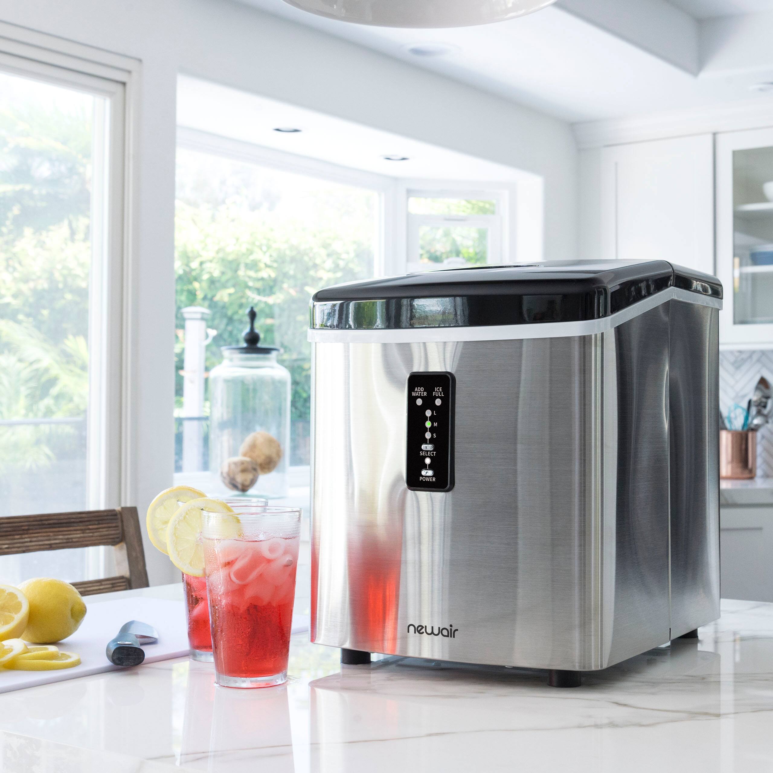 A newair ice machine is sitting on a counter next to a glass of pink liquid, which could be lemonade.
