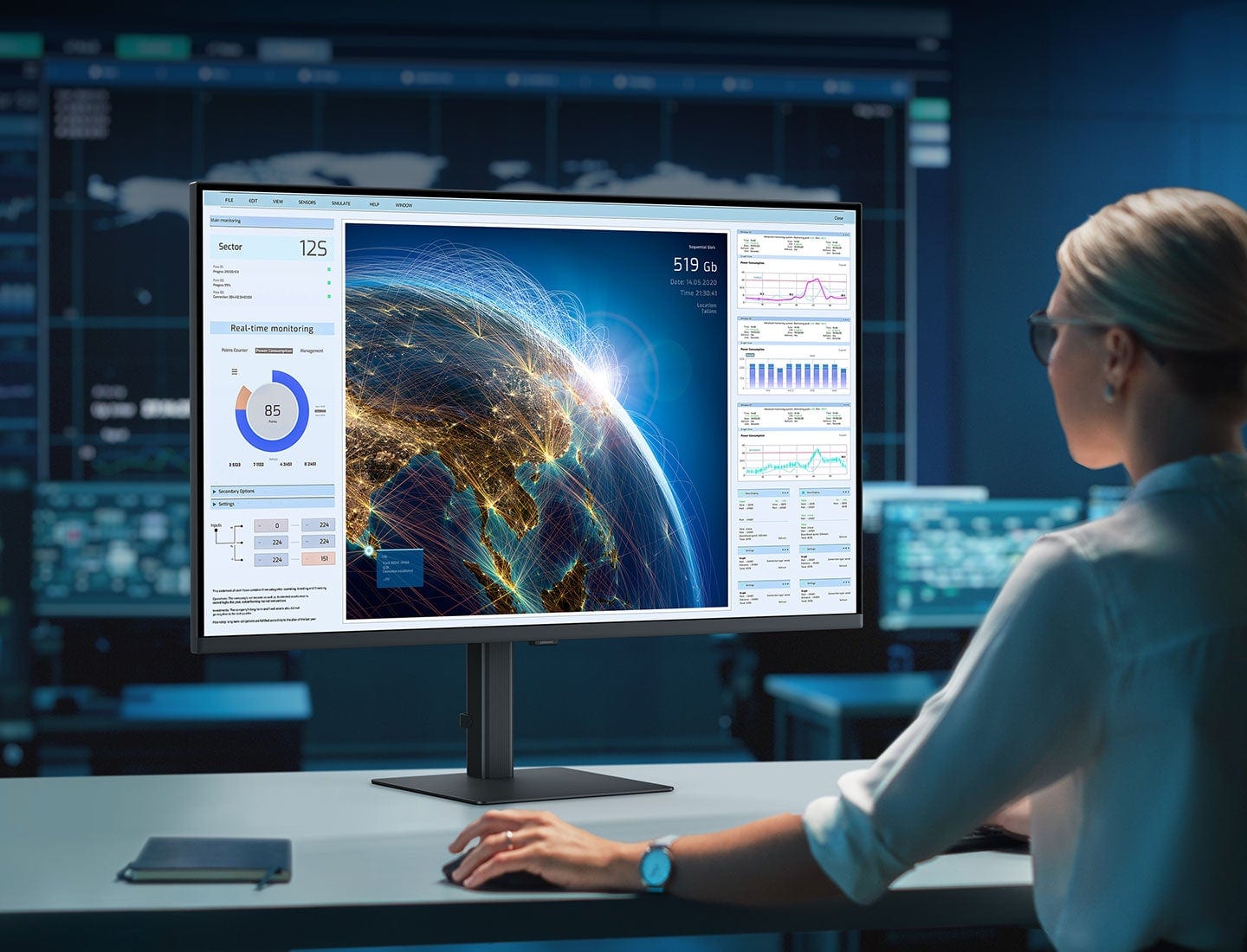 The text on the image reads: "Sector 125 519 Gb -ee 14.24.2000 Pnse 3 Heal-time monitoring 85 - i - -- smg - 1 I in i 2 -". This text is likely related to the image of a woman sitting at a desk in front of a computer monitor, as it might be a description or information about the content displayed on the monitor. However, without more context or understanding of the image, it is difficult to group and correct the text accurately.