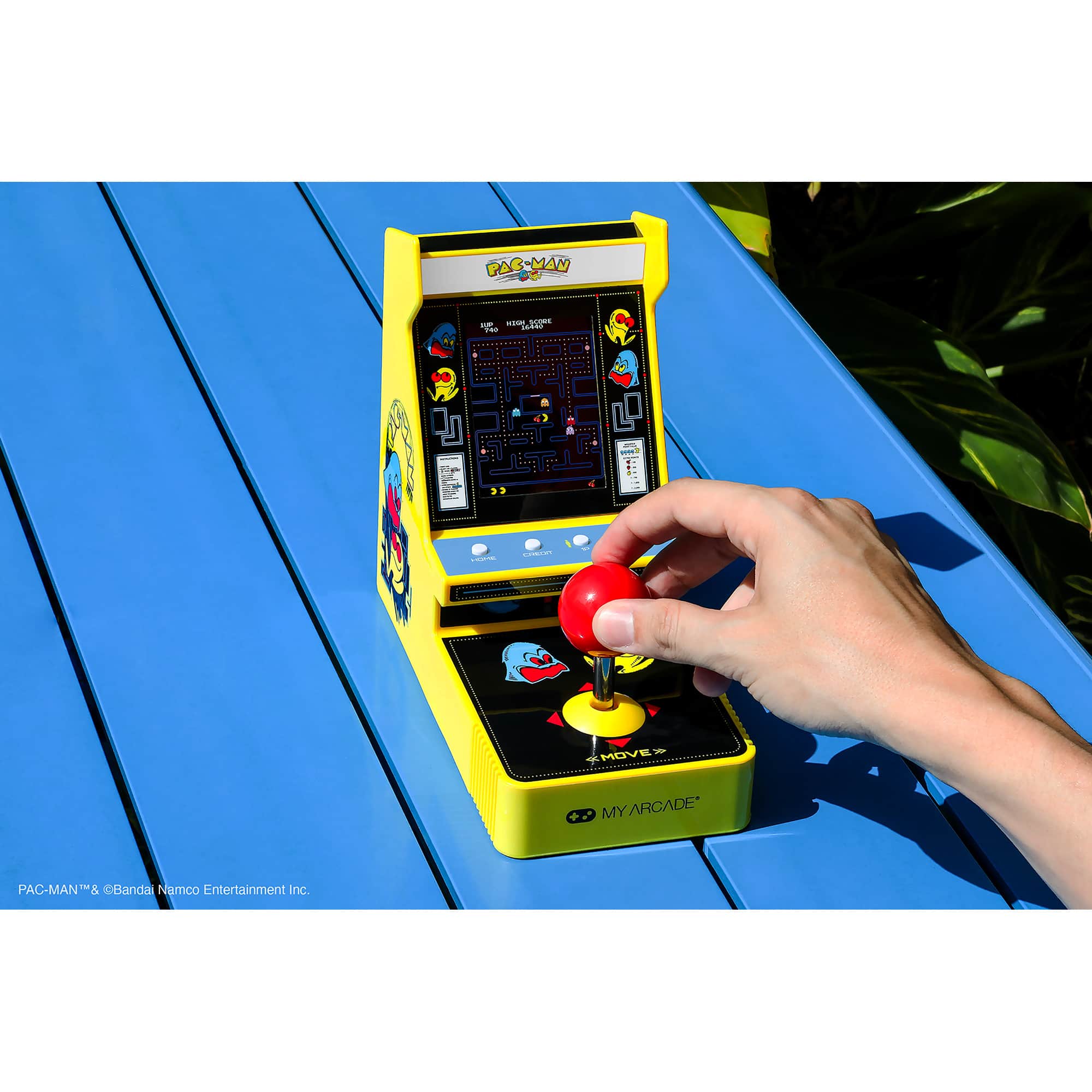 PAC-MAN is a popular game that has been adapted for the Nintendo Gameboy. In the image, a person is playing the game on a yellow machine, which is placed on a blue table. The game is a classic arcade game that has been adapted for home use, allowing players to enjoy the game in the comfort of their own homes. The person in the image is holding a red button, which is likely used to control the game. The game is a fun and engaging way to pass the time, and it is a great example of how classic arcade games can be adapted for modern gaming systems.