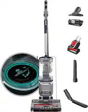 The image features a Shark vacuum cleaner and its attachments. The vacuum cleaner is positioned in the center of the image, with a scrubber and a brush located to the right of it. There is also a small circular item, possibly a cleaning tool, placed to the left of the vacuum cleaner. The scene showcases the various components of the Shark vacuum cleaner and its accessories.