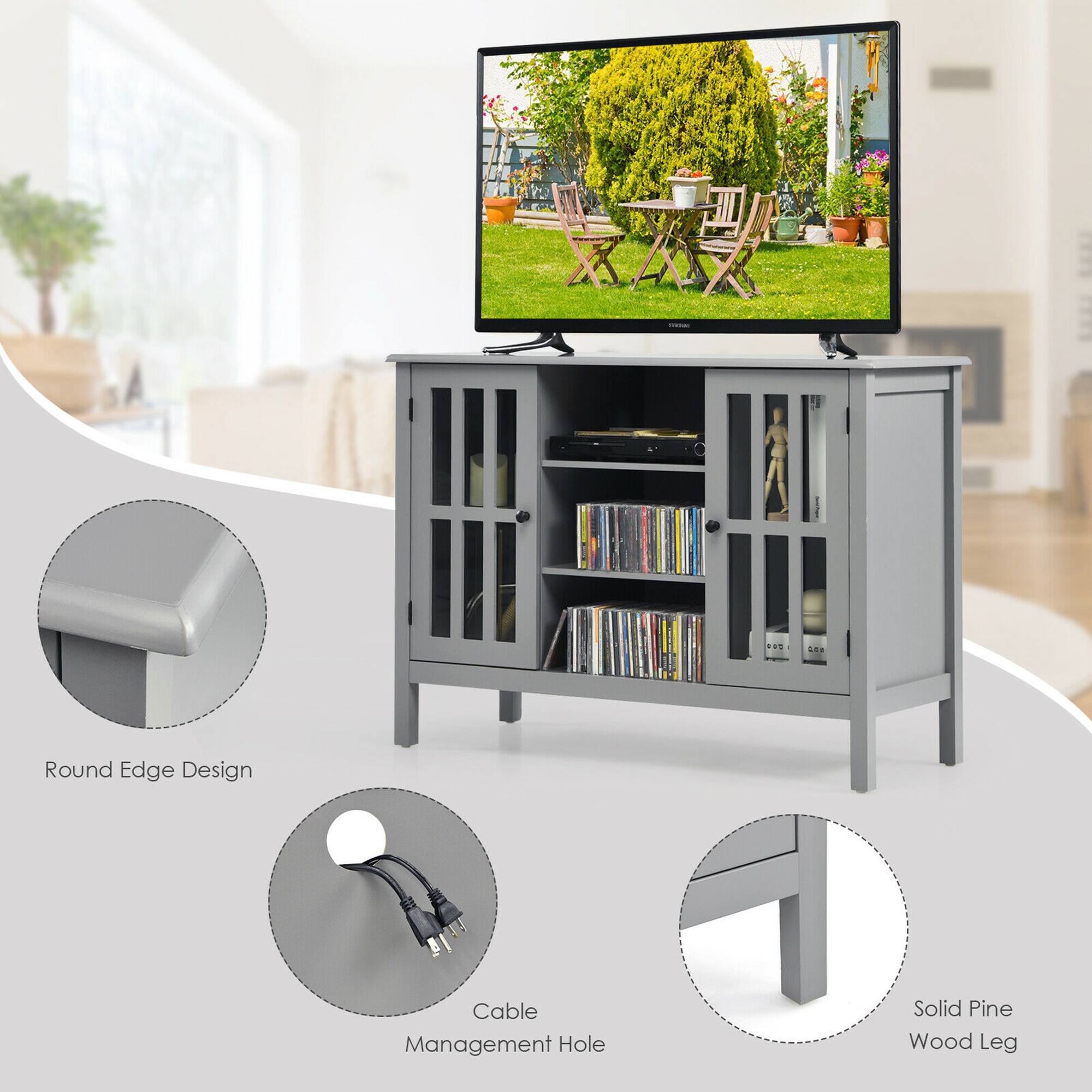 The image features a television stand with a television on top of it. The stand has a round edge design and a cable management hole. It also has a solid pine wood leg. The television is turned on, displaying a garden scene. The stand is placed in a living room, and there are multiple chairs in the room.