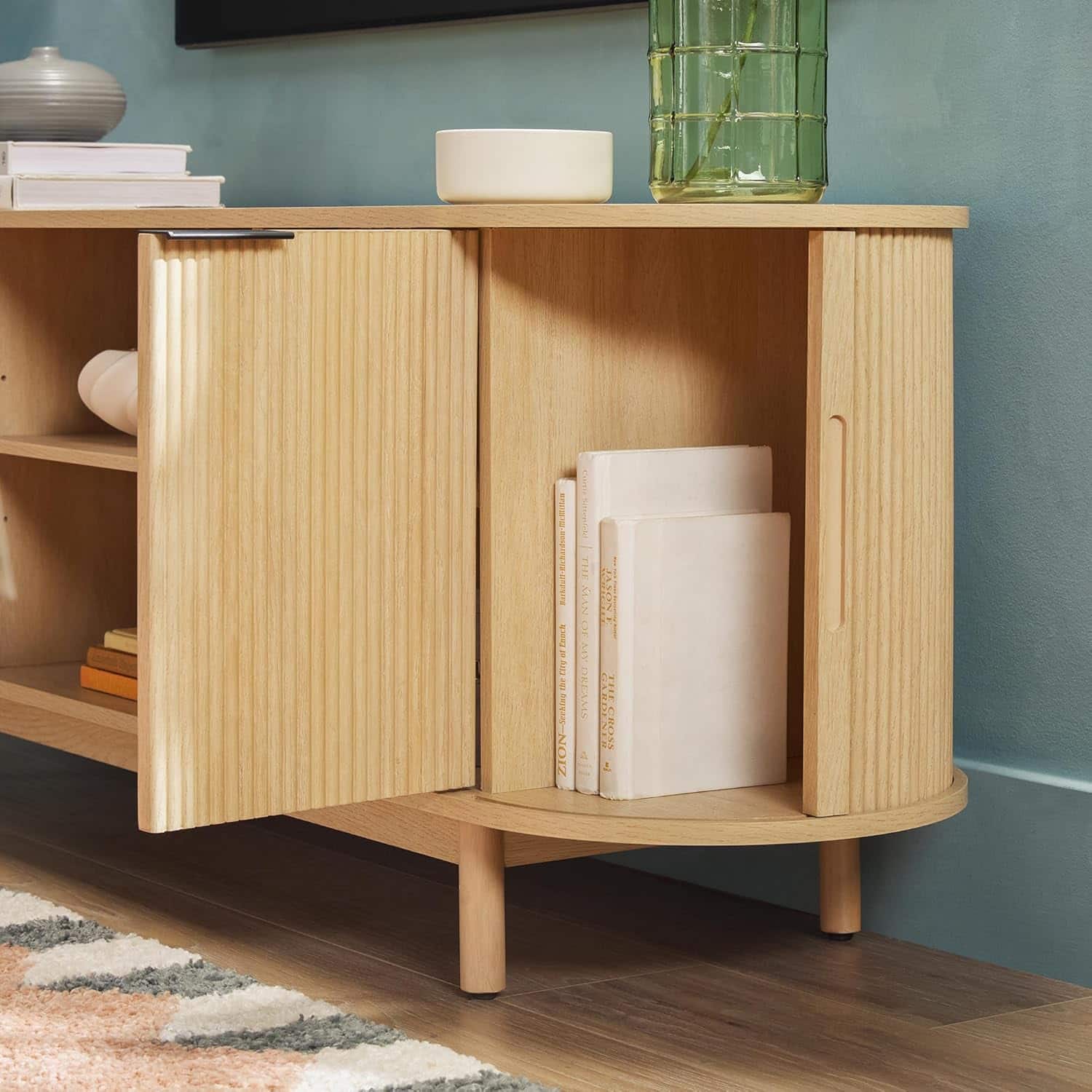 The text on the image is a jumble of words, making it difficult to group and correct. However, I can provide a brief description of the image:
The image features a wooden bookshelf with a variety of books and decorative items. There are several books of different sizes placed on the shelf, and a vase is also visible on the shelf. The bookshelf is situated in a room with a blue wall, and there is a rug on the floor.