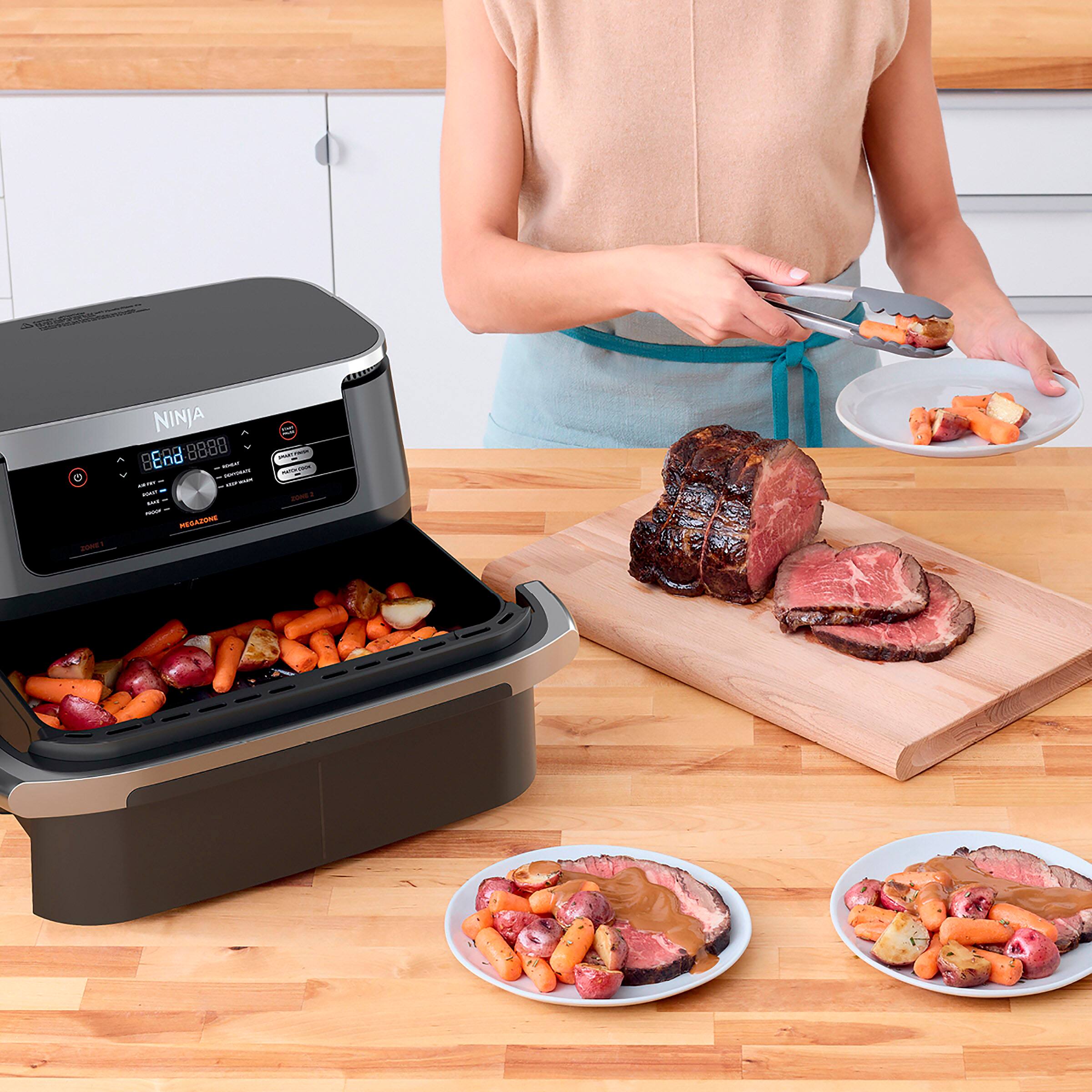 The image features a woman using a Ninja food processor to cook food. She is standing next to a cutting board with raw meat on it, and there are plates of food on the counter. The food processor is filled with vegetables, which are being cooked in the appliance. The woman is actively engaged in preparing the meal, ensuring that the food is cooked to perfection.