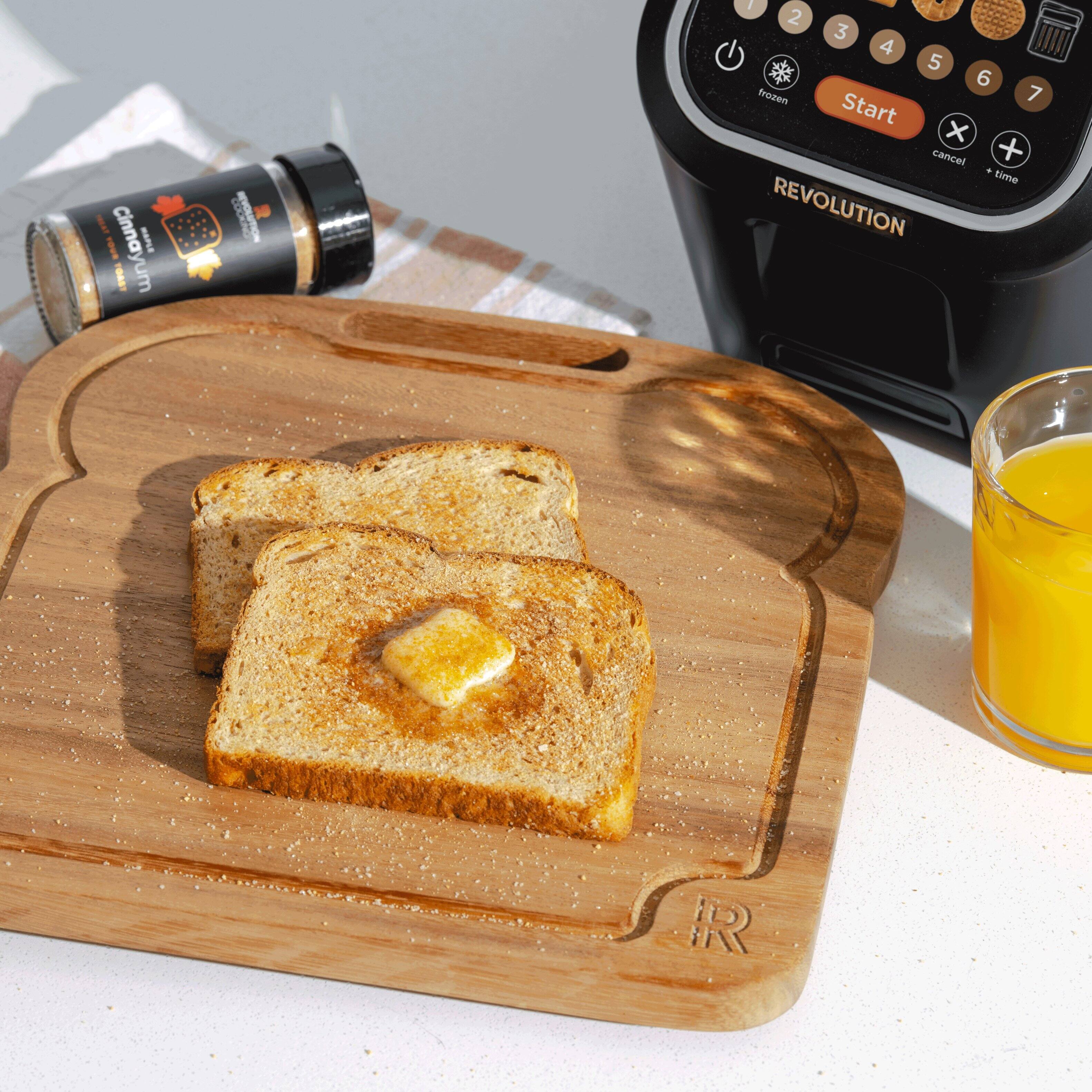 The image shows a toaster and a glass of orange juice on a table. The toaster is placed on the left side of the table, while the glass of orange juice is on the right side. There is also a cutting board with two slices of toast on it, placed in the middle of the table. The toast has butter on it, making it a delicious and healthy breakfast option.