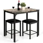The image features a table with two black stools and a bottle of wine. There are two wine glasses on the table, one near the left stool and the other near the right stool. The table is accompanied by a potted plant, adding a touch of greenery to the scene. The arrangement creates a cozy and inviting atmosphere for enjoying a glass of wine.