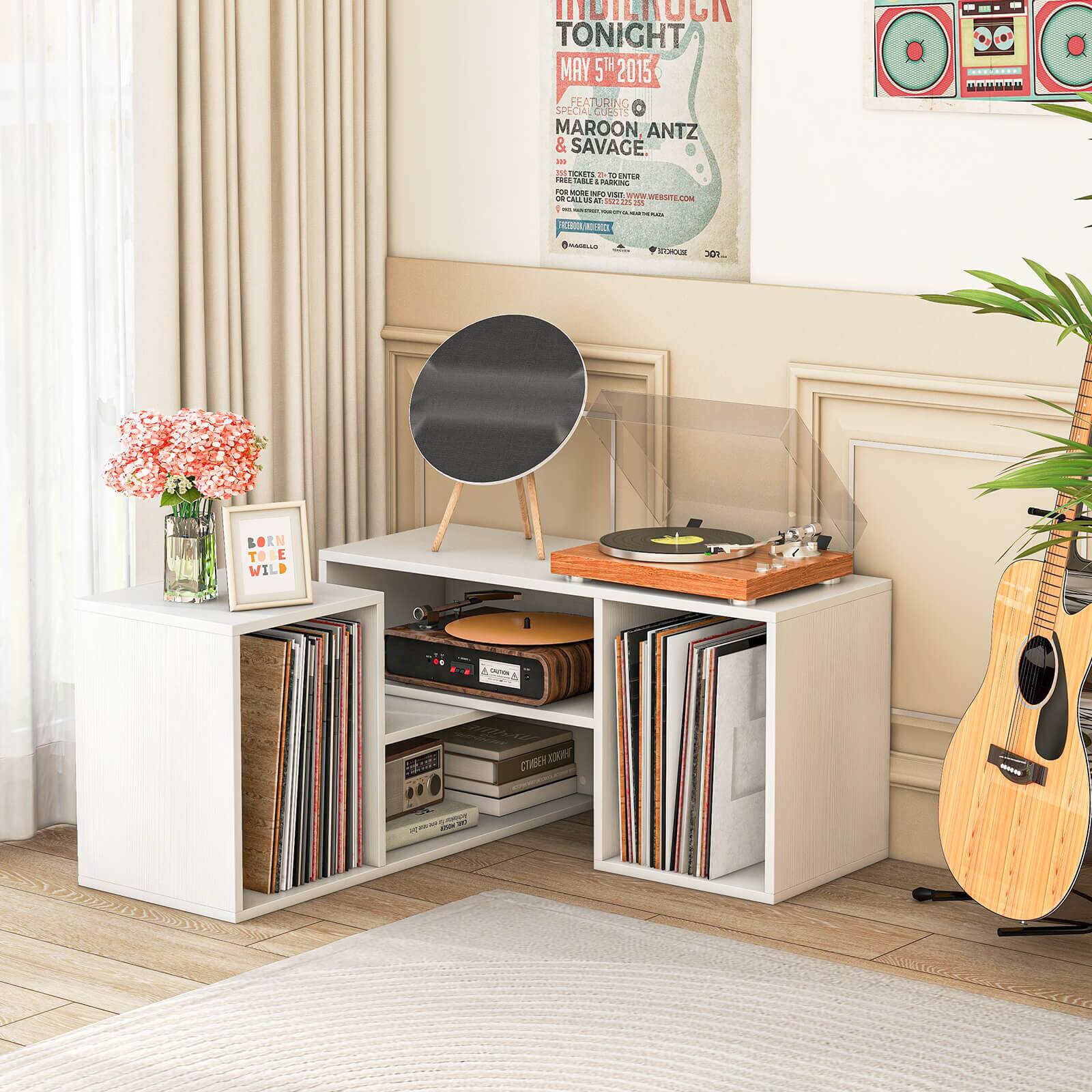 The image features a white table with a record player and a poster advertising a concert on May 5, 2015. The poster also includes the names of the special guests, Maroon, Antz, and Savage. The table also has a guitar on it, and there are several books and records placed on the table. Additionally, there is a potted plant nearby, adding a touch of greenery to the scene.