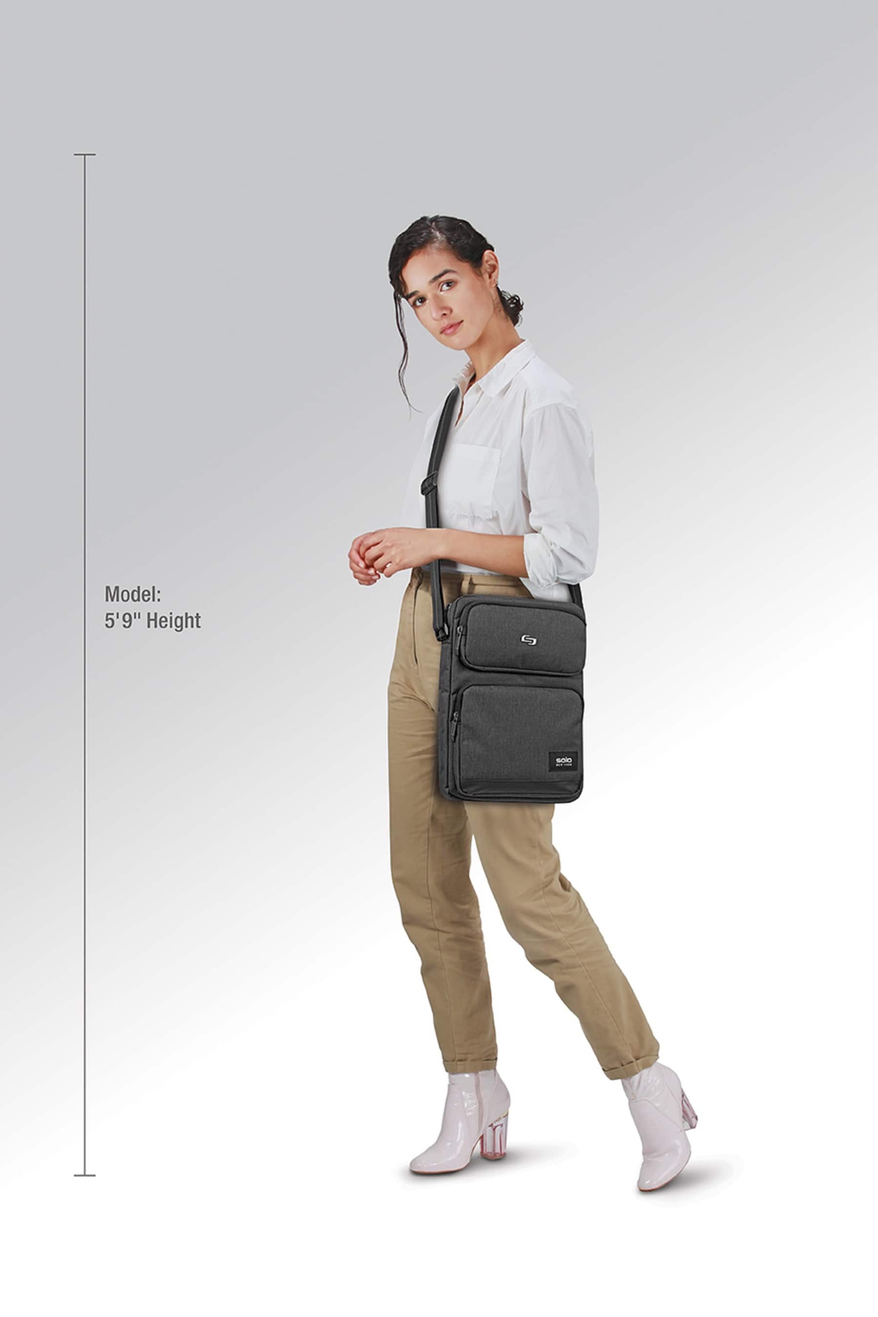The image features a woman standing and wearing a black bag. She is also wearing a white shirt and pants. The woman is holding a black bag, which is likely a purse. The image is likely a model photo, as it is described as a "model" and "model photo." The woman's height is given as 5'9".