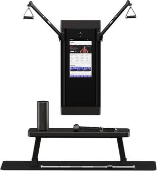 The image features a large black electronic device, possibly a television or a computer monitor, mounted on a wall. The device is displaying a man on the screen. The wall also has a scale mounted on it, which is likely used for measuring weight. The overall setting appears to be a gym or a fitness center, as the presence of the scale suggests a focus on health and fitness.