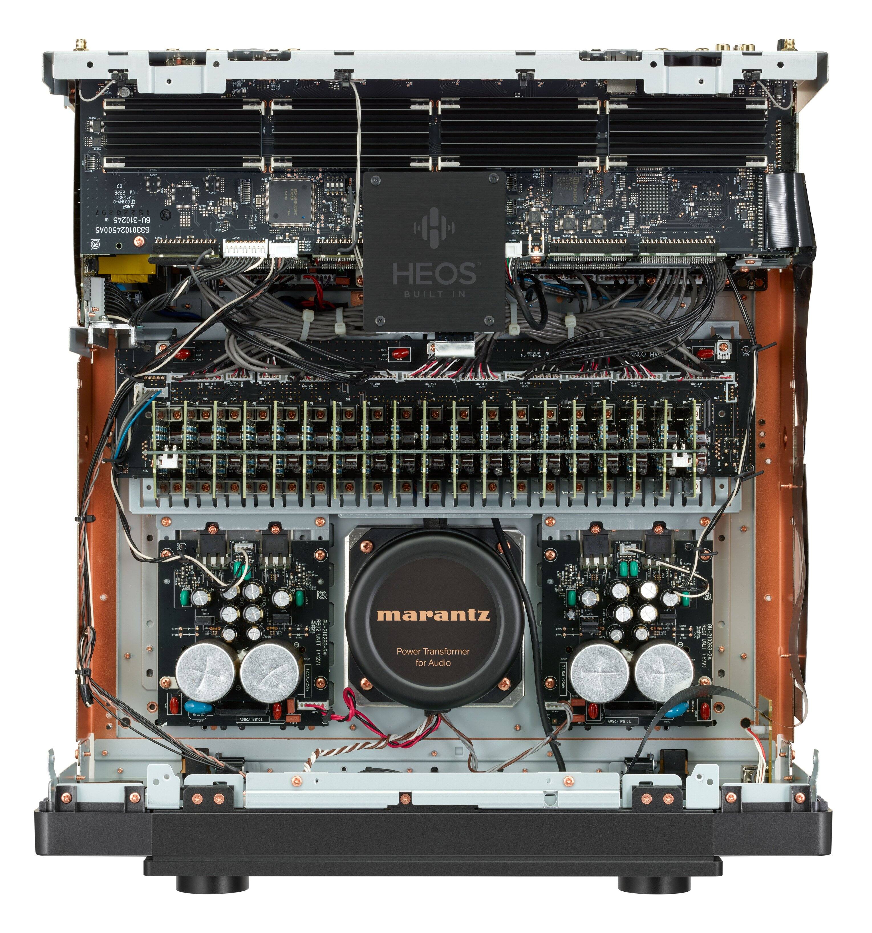 The image features a Marantz device with a power transformer for audio. The device is equipped with a built-in HEOS system, which is designed for high-quality sound. The back of the device is open, revealing the internal components, including the power transformer. The device is likely used for amplifying audio signals, providing a better listening experience.
