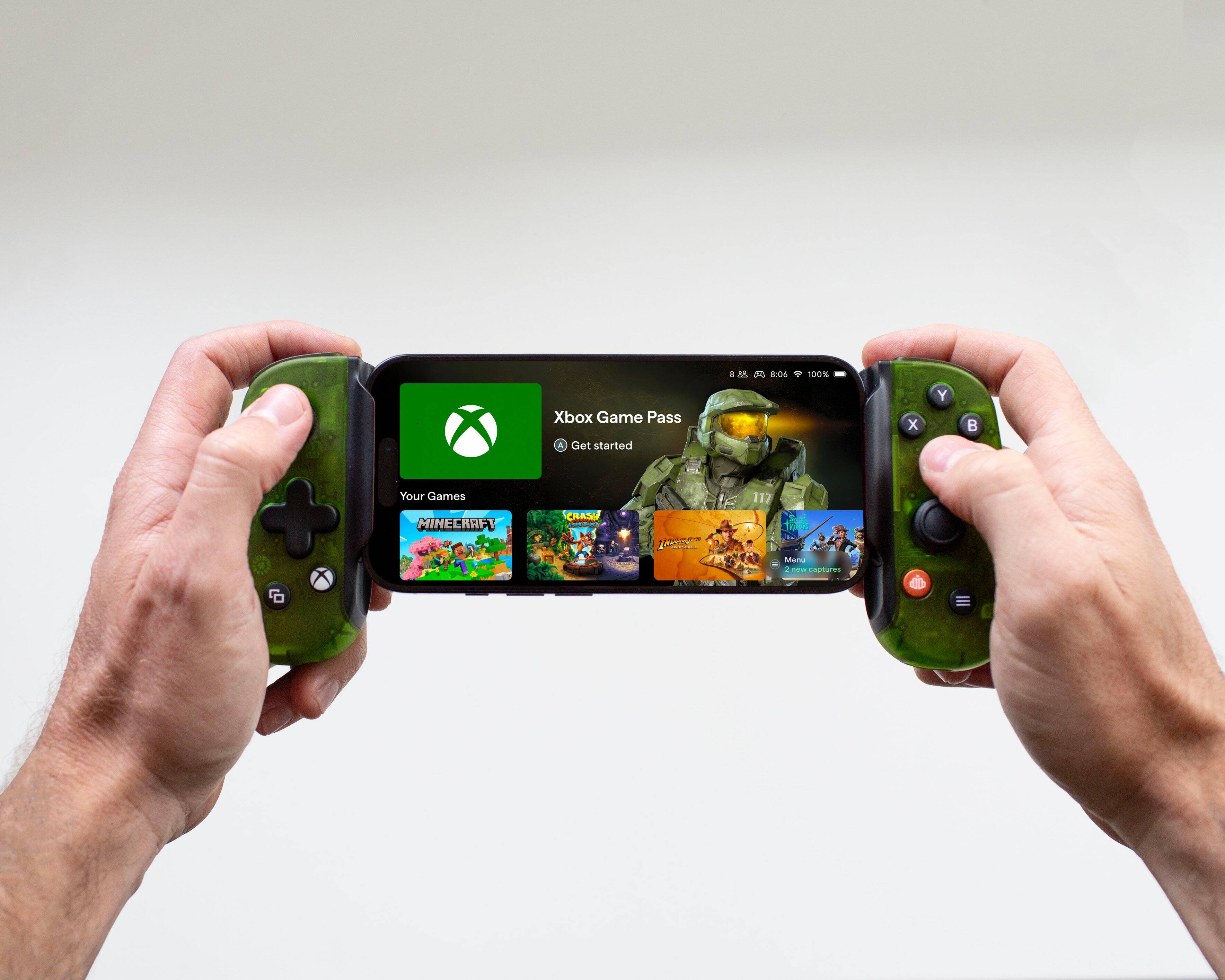 A person is holding a cell phone with a green controller on their hand. The cell phone is displaying the Xbox Game Pass app, which offers a 100% discount for new subscribers. The app also features a picture of a Minecraft character on the screen.