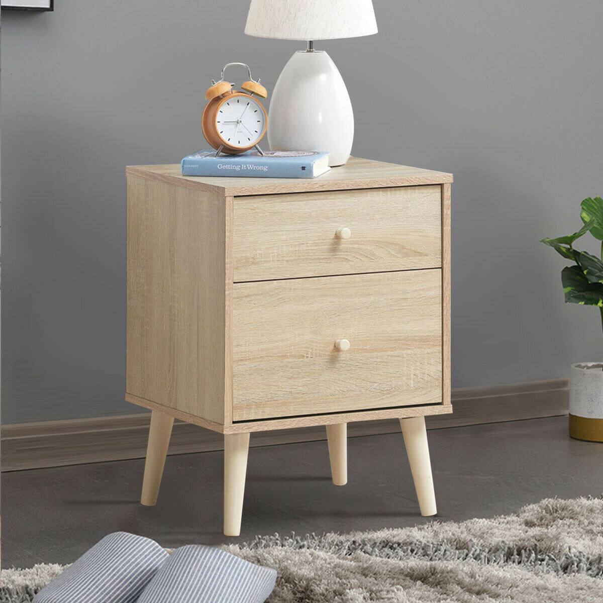 The image shows a wooden nightstand with a clock and a lamp on it. The clock is placed on the left side of the nightstand, while the lamp is positioned on the right side. The nightstand is situated on a carpeted floor, and there is a book placed on the left side of the nightstand as well.