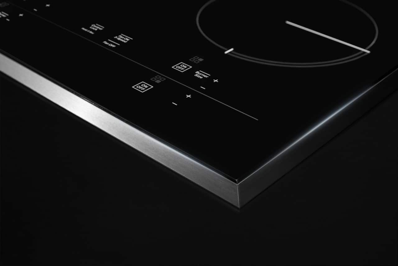 The image features an electric cooktop with a large knob on the left side and a smaller knob on the right side. The knobs are used to control the heat settings for the burners. The cooktop is black and silver in color, and the knobs are clearly visible in the image. The knobs are likely used to adjust the temperature of the burners, allowing for precise cooking control.