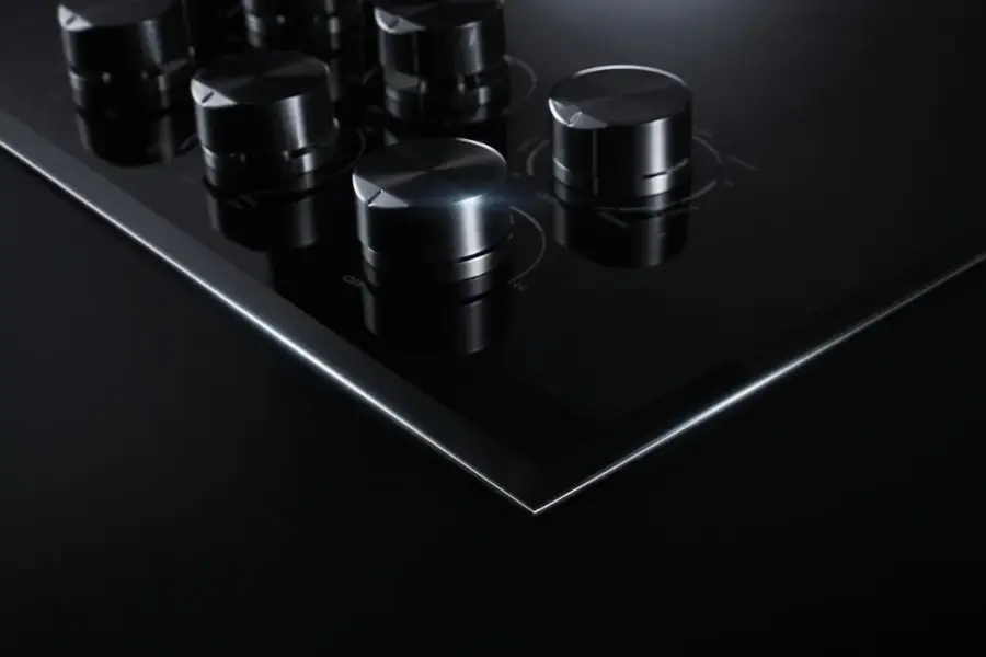 The image features a black electric cooktop with a square design and a row of knobs. The cooktop is placed on a black countertop, giving it a sleek and modern appearance. The knobs are arranged in a neat line, and their size and positioning contribute to the overall aesthetic of the cooktop. The image is categorized as Electric_Cooktops, which highlights the type of cooking appliance displayed in the photo.