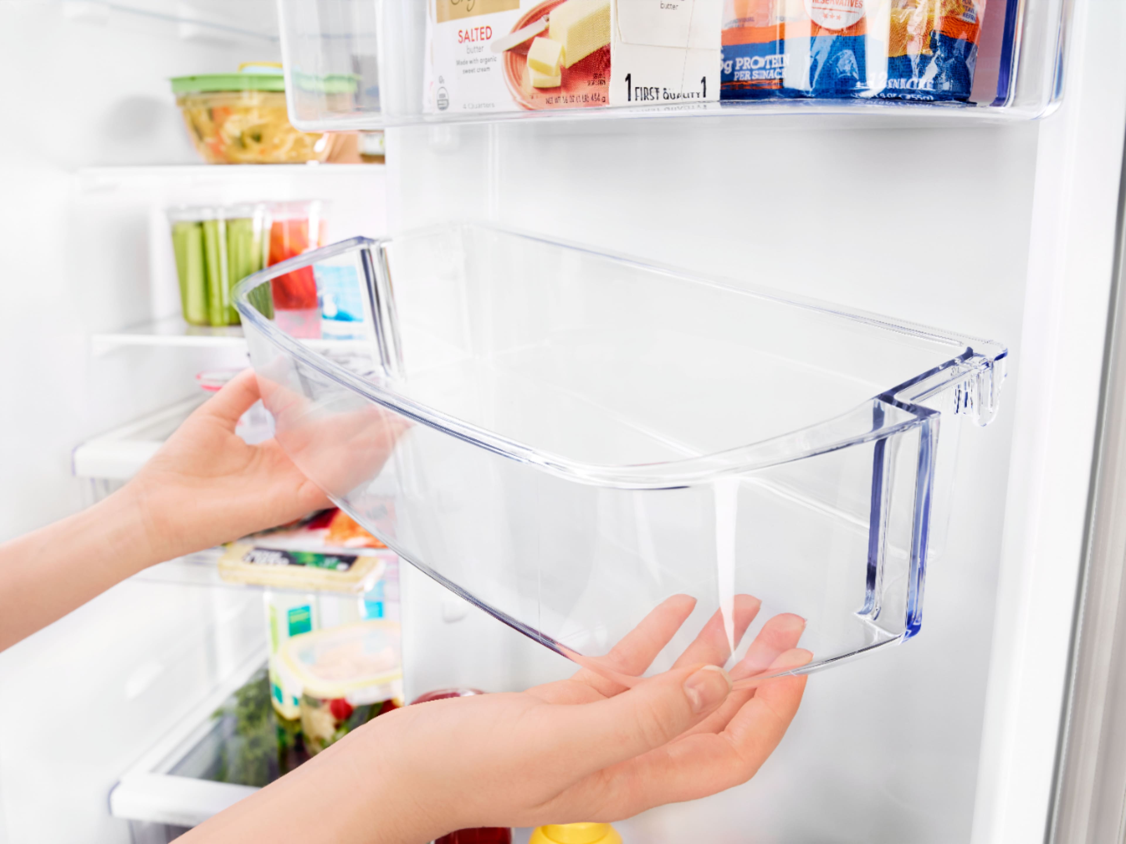 The image features a large white refrigerator with its door open, revealing a variety of food items inside. There are several bottles, including a bottle of juice, and a box of ice cream. Additionally, there are multiple carrots placed in the refrigerator, possibly for a healthy snack. The refrigerator is well-stocked and ready for use.