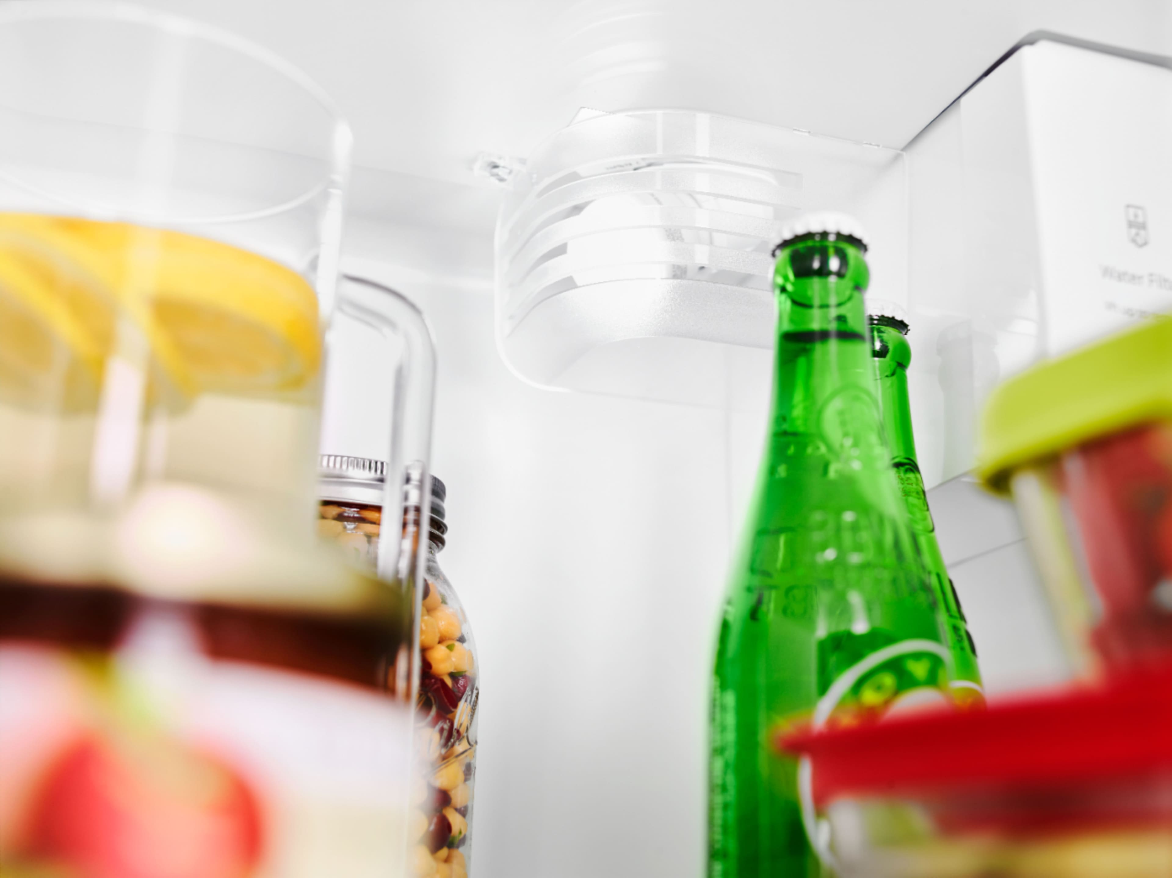 The image features a person holding a clear plastic container, likely a glass bowl, out of a refrigerator. The refrigerator is filled with various food items, including bottles and a cup. The person is standing in front of the refrigerator, which is open, and they are holding the container with their hand.