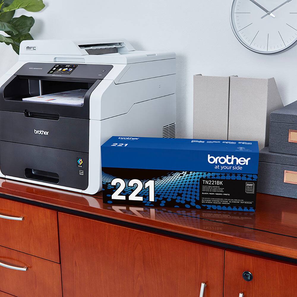 The image features a printer and a box of toner cartridges. The printer is a Brother MFC-221, and the toner cartridges are specifically designed for this model. The box of toner cartridges is placed next to the printer, indicating that they are ready to be used. The presence of the printer and toner cartridges suggests that the user is well-prepared for their printing needs.