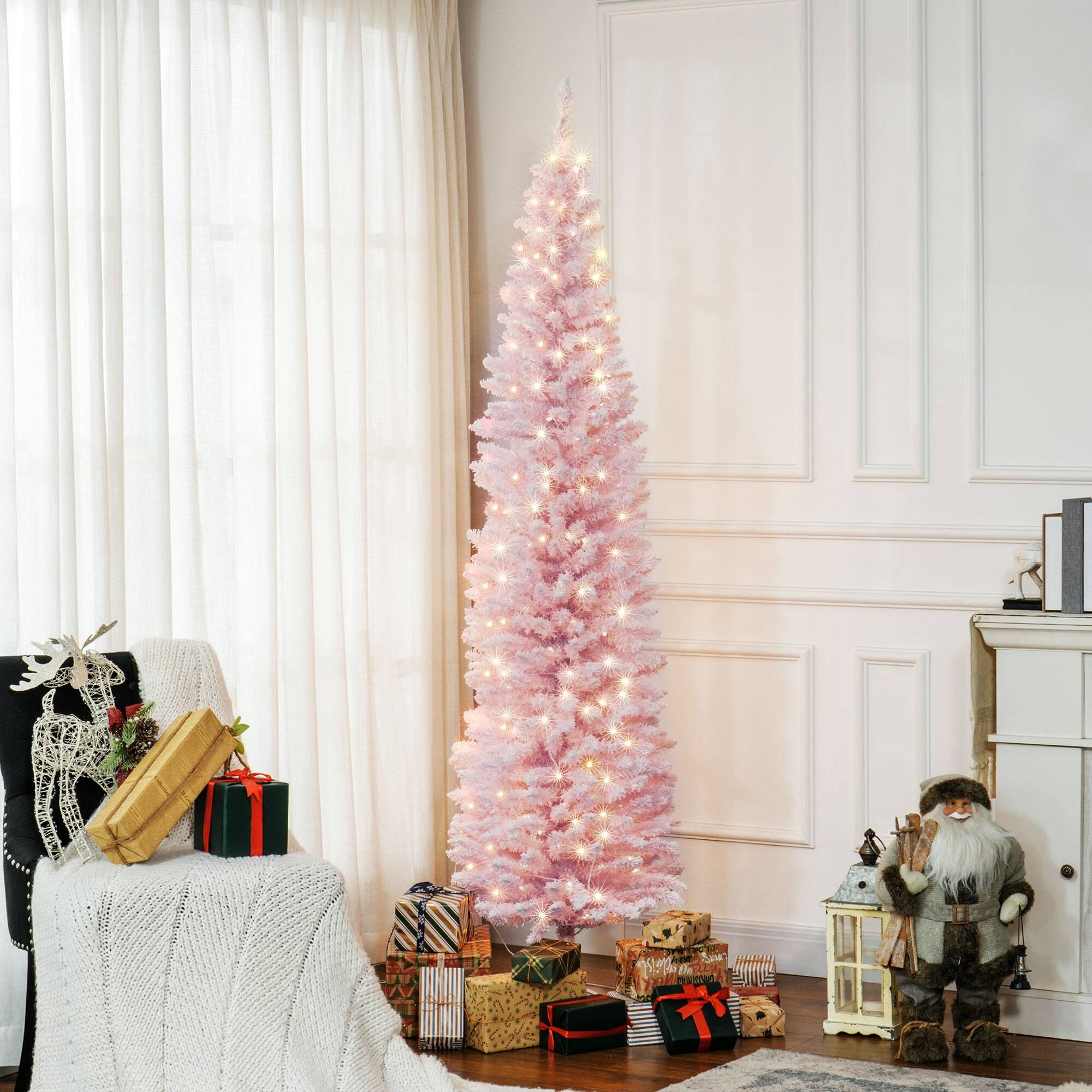 The image shows a festive scene with a pink Christmas tree adorned with white lights. The tree is surrounded by various wrapped gifts with colorful ribbons. To the left, there is a chair draped with a white knitted blanket, and a reindeer decoration is placed on it. On the right, a Santa Claus figure stands next to a lantern. The background features a white wall and a window with sheer curtains.