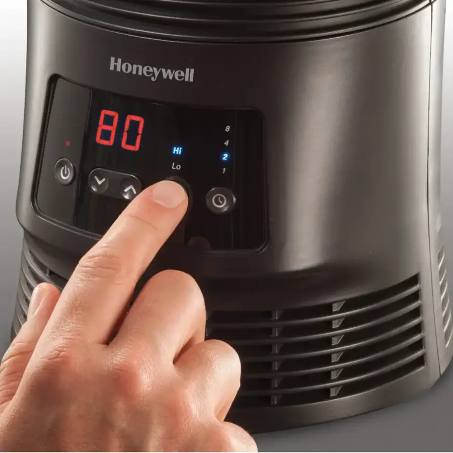 The image shows a person's hand pressing a button on a Honeywell heater. The button is labeled "80" and is located on the front of the heater. The person's hand is positioned over the button, indicating that they are adjusting the temperature setting on the heater.