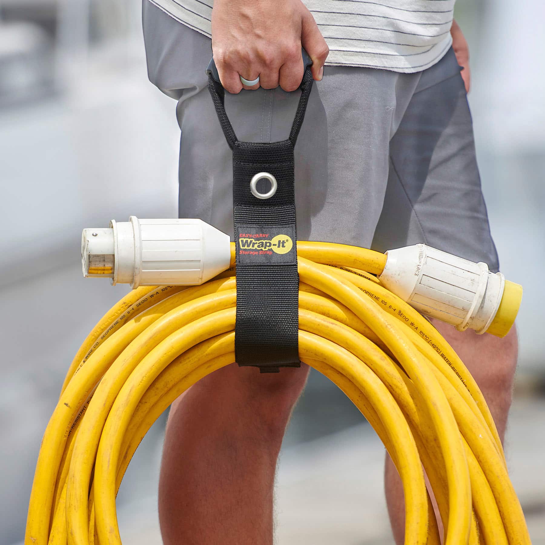 The text on the image reads "FATCLRRT Wrap-It Storage deuis K% HEAE E -E UM PP NT K20 RENE 1 04 SEDO W-A cL 1Tn eoc hri war." This text is likely a description or instructions for using the yellow hose and the black strap.