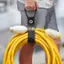 The text on the image reads "FATCLRRT Wrap-It Storage deuis K% HEAE E -E UM PP NT K20 RENE 1 04 SEDO W-A cL 1Tn eoc hri war." This text is likely a description or instructions for using the yellow hose and the black strap.