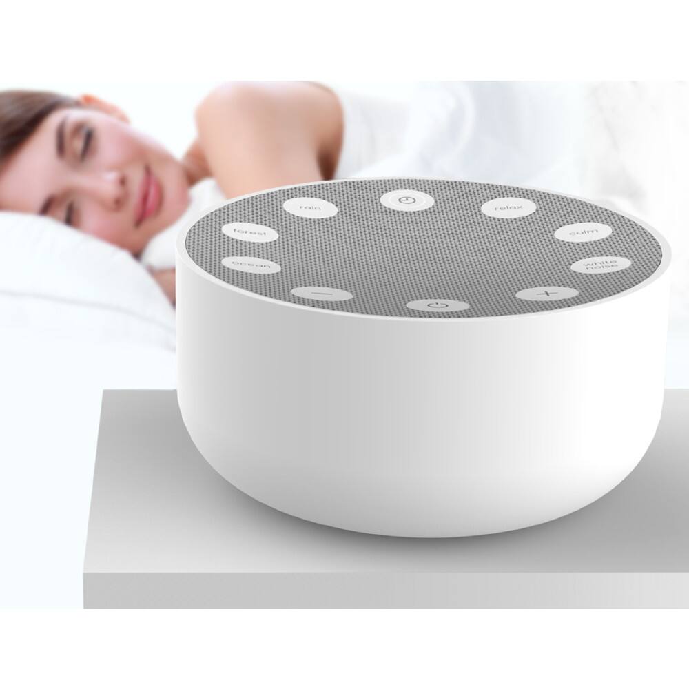 The image shows a woman lying in bed next to a white speaker. The speaker is placed on a table, and it has buttons on it. The woman appears to be sleeping, and the scene suggests a relaxing and peaceful atmosphere.