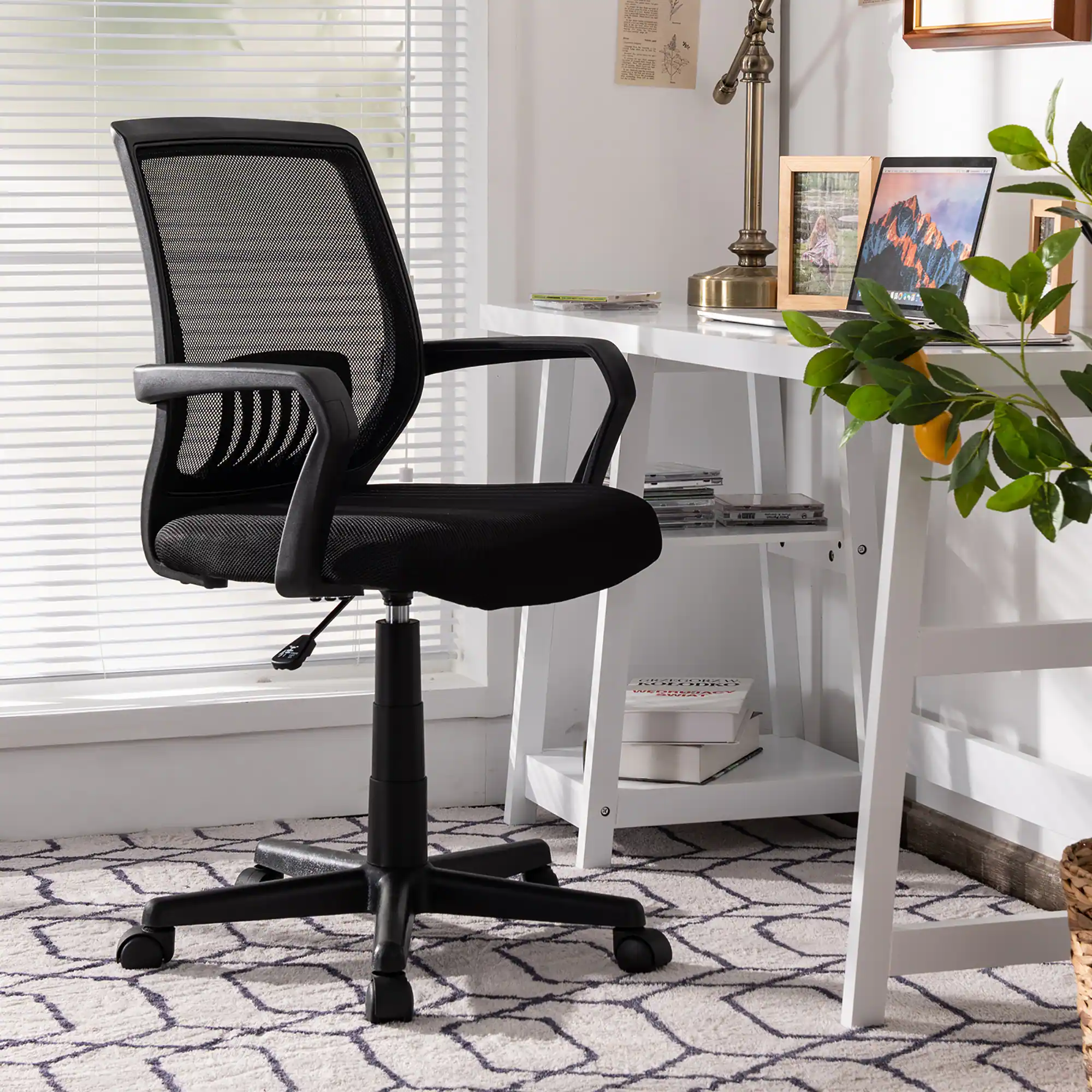 The image features a black office chair with wheels, positioned in front of a desk. The desk has a laptop and a keyboard on it. There is also a book on the desk, and a potted plant is placed nearby. The scene appears to be a home office setup.