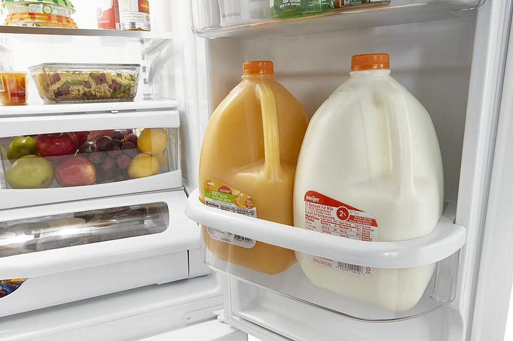 The image displays a refrigerator with two gallons of orange juice and a gallon of milk. The refrigerator is filled with various food items, including apples, oranges, and other fruits. The orange juice is placed on the top shelf, while the milk is positioned on the bottom shelf. The refrigerator is well-stocked, providing a variety of options for meals and snacks.