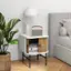 The image features a nightstand with a lamp, a radio, and a book. The lamp is turned on, and the radio is sitting on the nightstand. There is also a book on the nightstand, and a bed is visible in the background. The scene is set in a bedroom, with a potted plant nearby, adding a touch of greenery to the space.