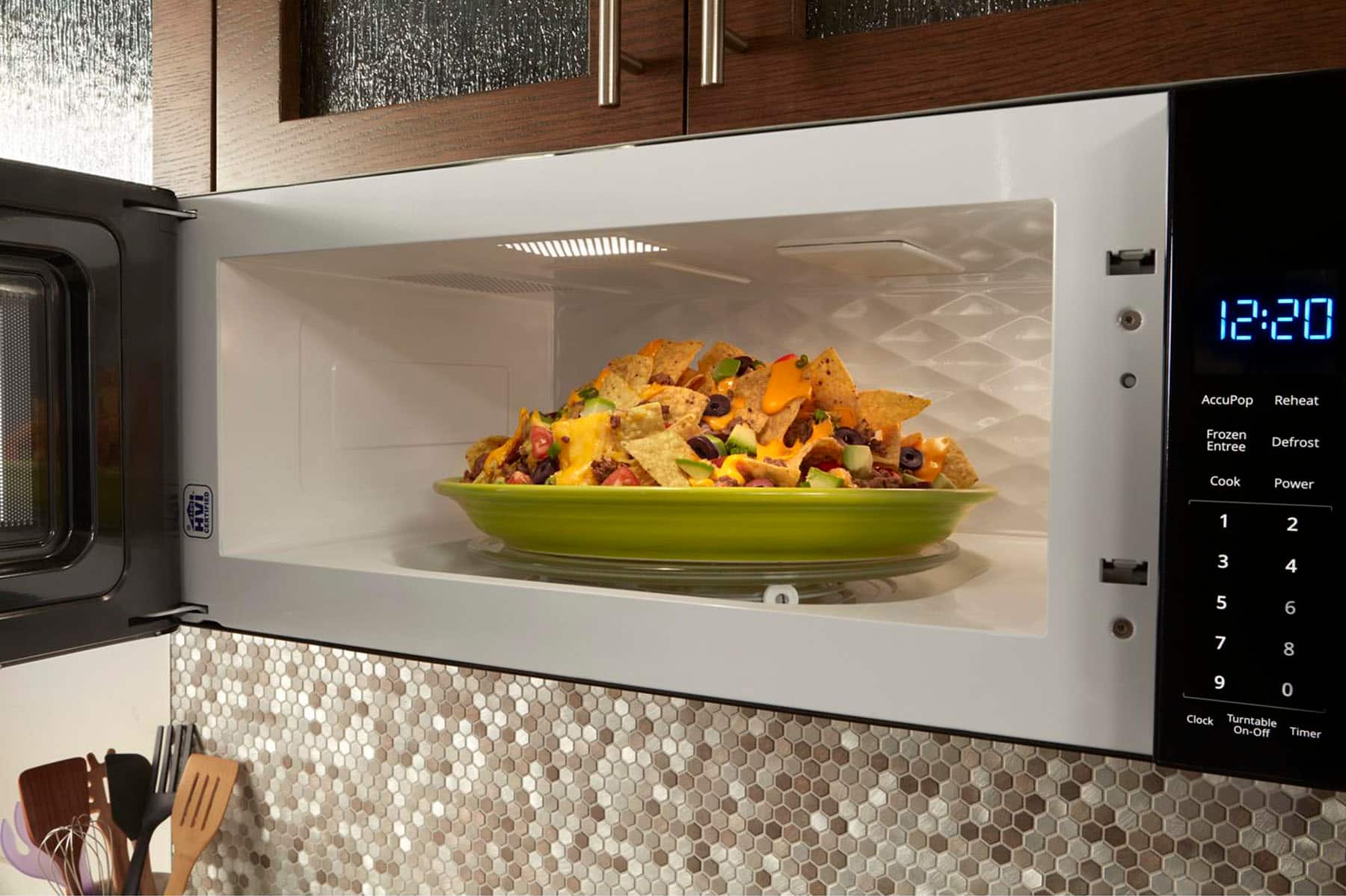 The image shows a microwave with a bowl of food inside, which is set to cook at 12:20. The microwave is equipped with a clock, a turntable, and an on-off timer. The food in the bowl appears to be a frozen entree that has been defrosted and is now being reheated.