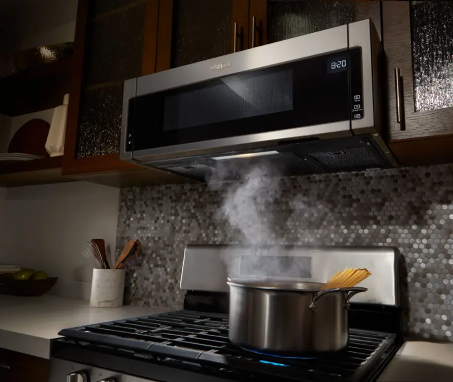 The image shows a microwave with a bowl of food inside, which is set to cook at 12:20. The microwave is equipped with a clock, a turntable, and an on-off timer. The food in the bowl appears to be a frozen entree that has been defrosted and is now being reheated.