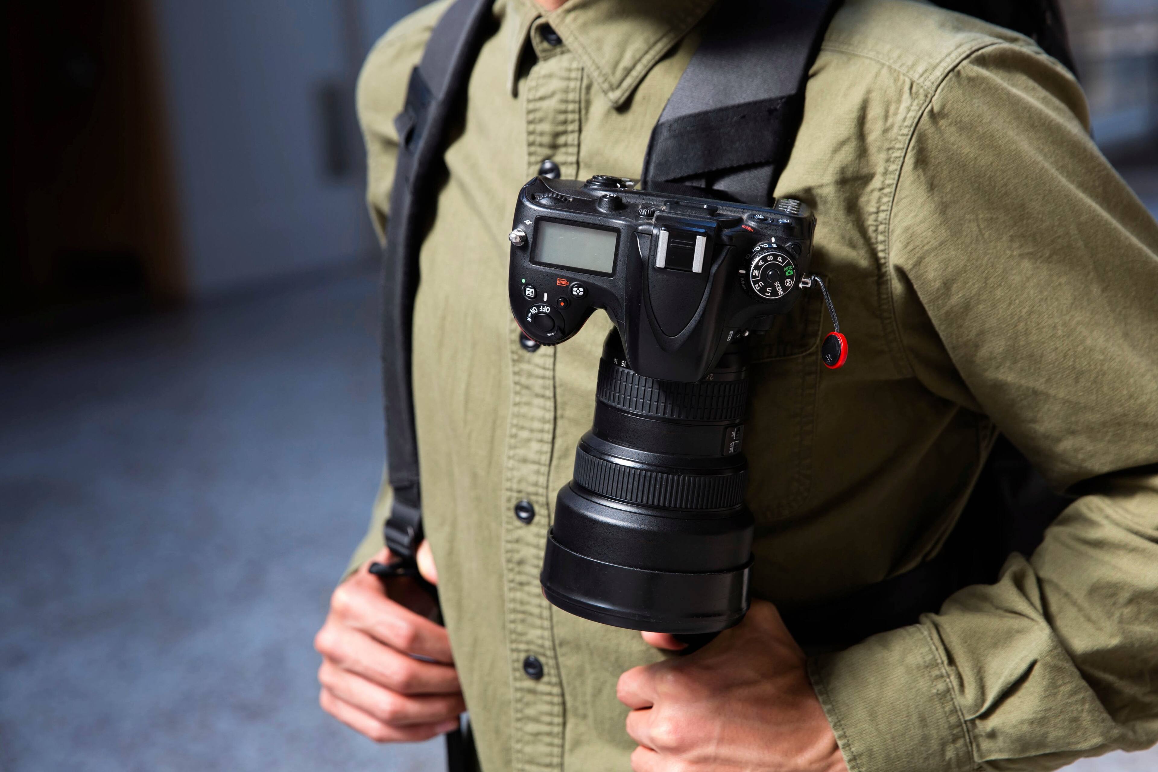 The person in the image is wearing a backpack and holding a camera in their hands. The camera is attached to the backpack, making it easy for the person to carry it around. The backpack is black, and the camera is large, indicating that it might be a professional or high-quality camera. The person is also wearing a green shirt, which complements the backpack and camera.