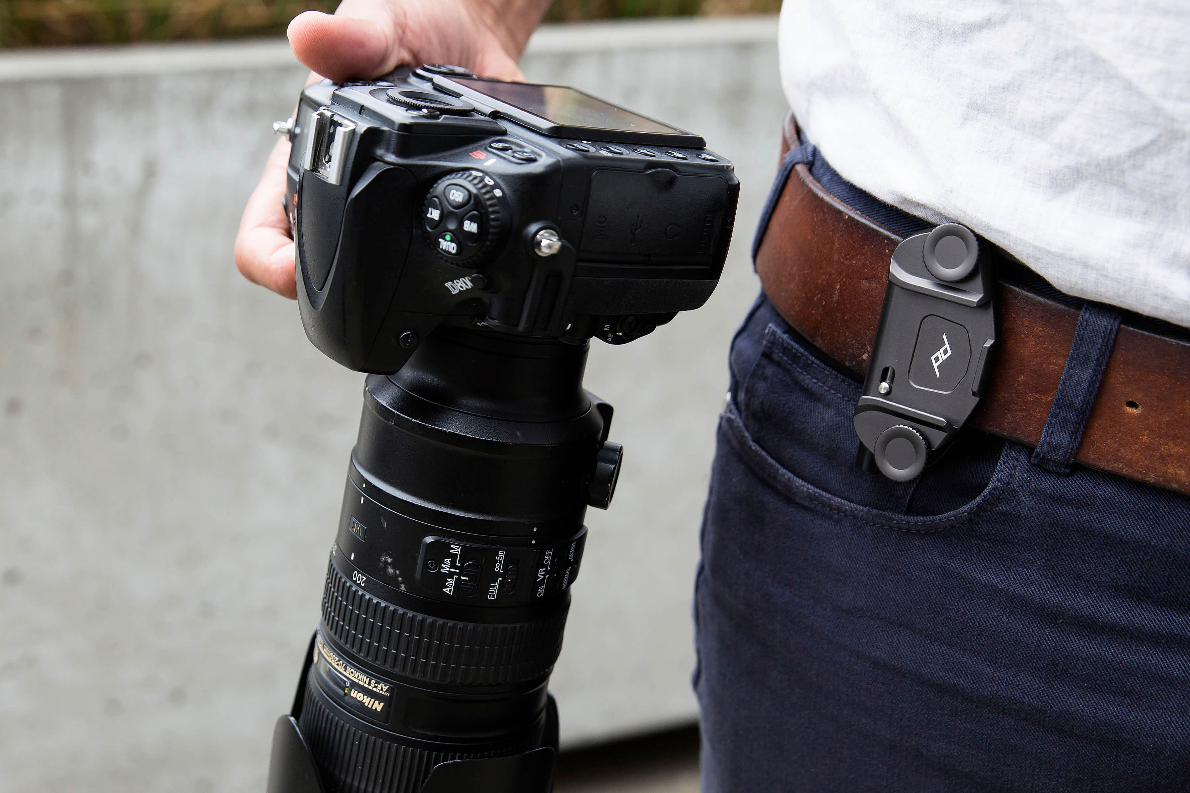 The image shows a person holding a camera and a cell phone in their hands. The camera is a Nikon D5200, and the cell phone is an iPhone. The person is wearing a belt with a camera case attached to it, which is a convenient way to carry the camera around. The image captures the essence of modern technology and photography, as the person is able to use both the camera and the cell phone for capturing memories and staying connected.