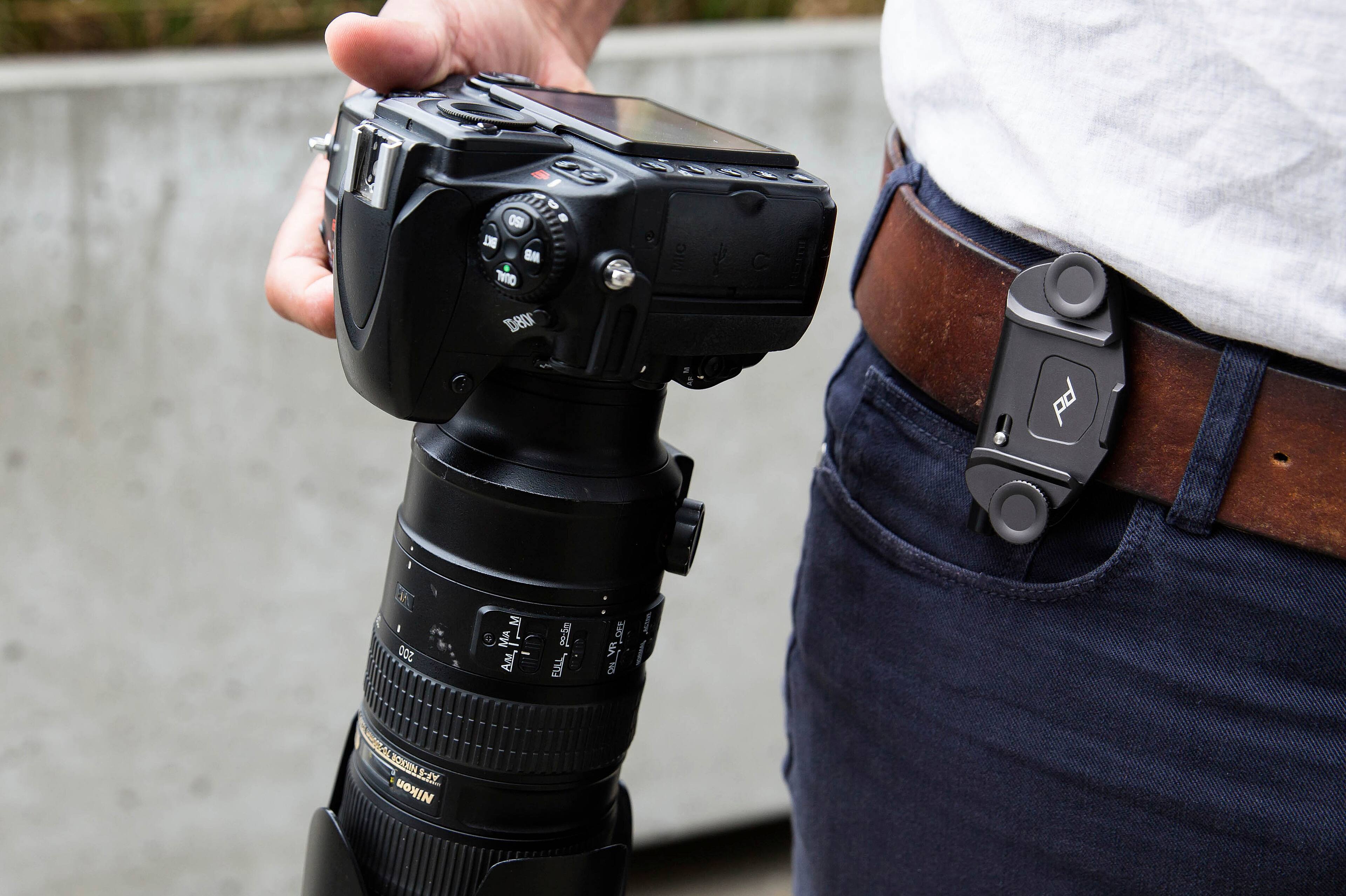 The image shows a person holding a camera and a cell phone in their hands. The camera is a Nikon D5200, and the cell phone is an iPhone. The person is wearing a belt with a camera case attached to it, which is a convenient way to carry the camera around. The image captures the essence of modern technology and photography, as the person is able to use both the camera and the cell phone for capturing memories and staying connected.