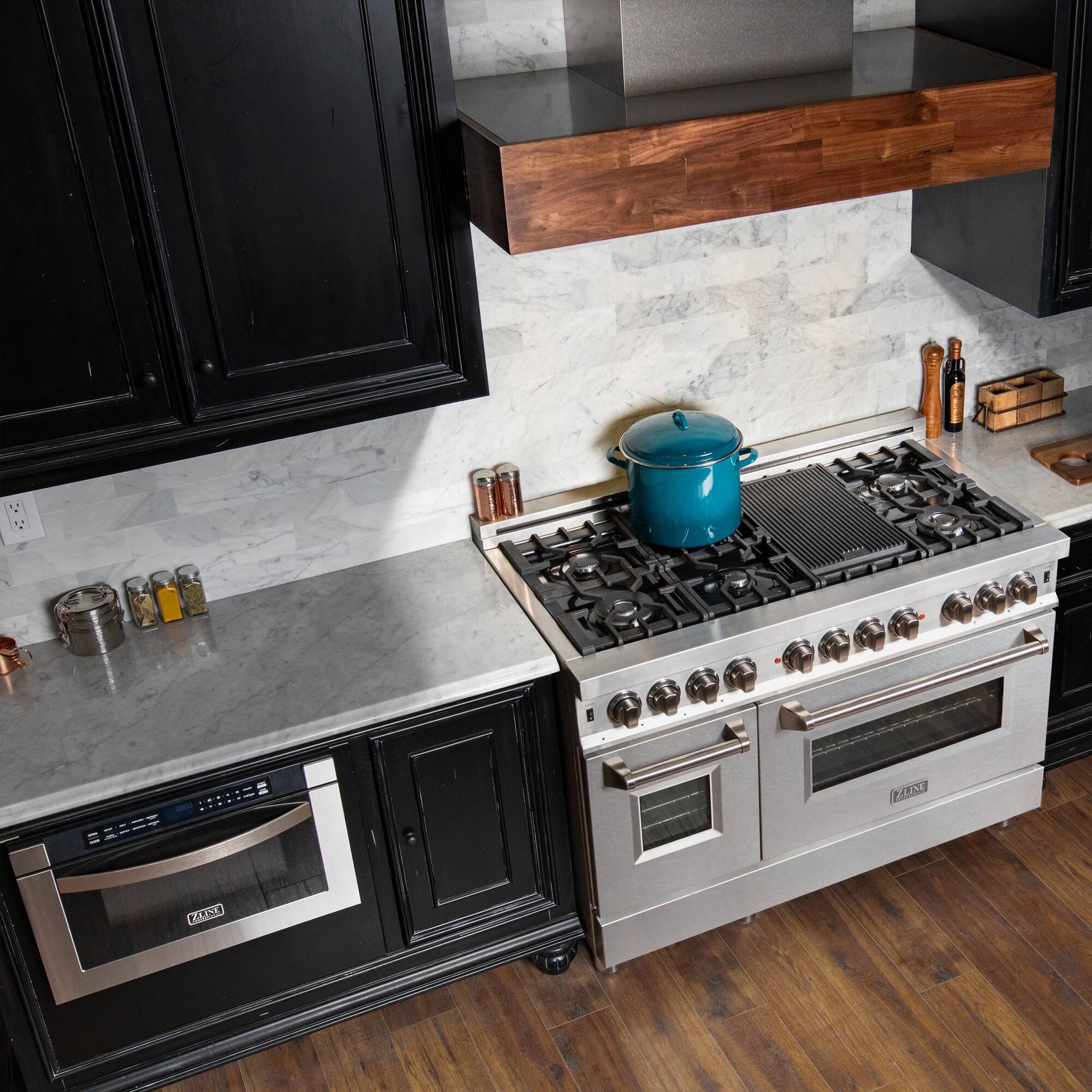 A modern kitchen with black cabinets, a stainless steel stove, and a blue pot on the counter.